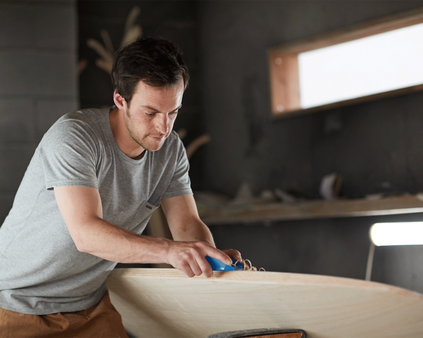 A person shaping and carving a wooden surfboard.
