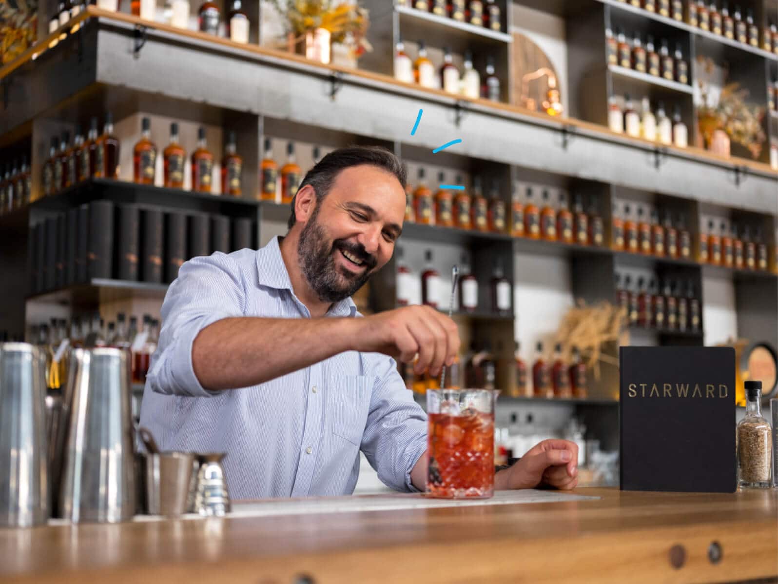 A man is behind a bar, smiling while pouring a drink.