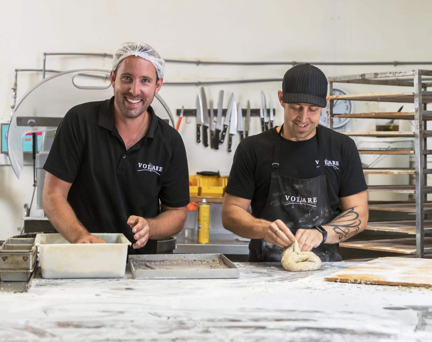 Two bakers working on a bench top and smiling at the camera