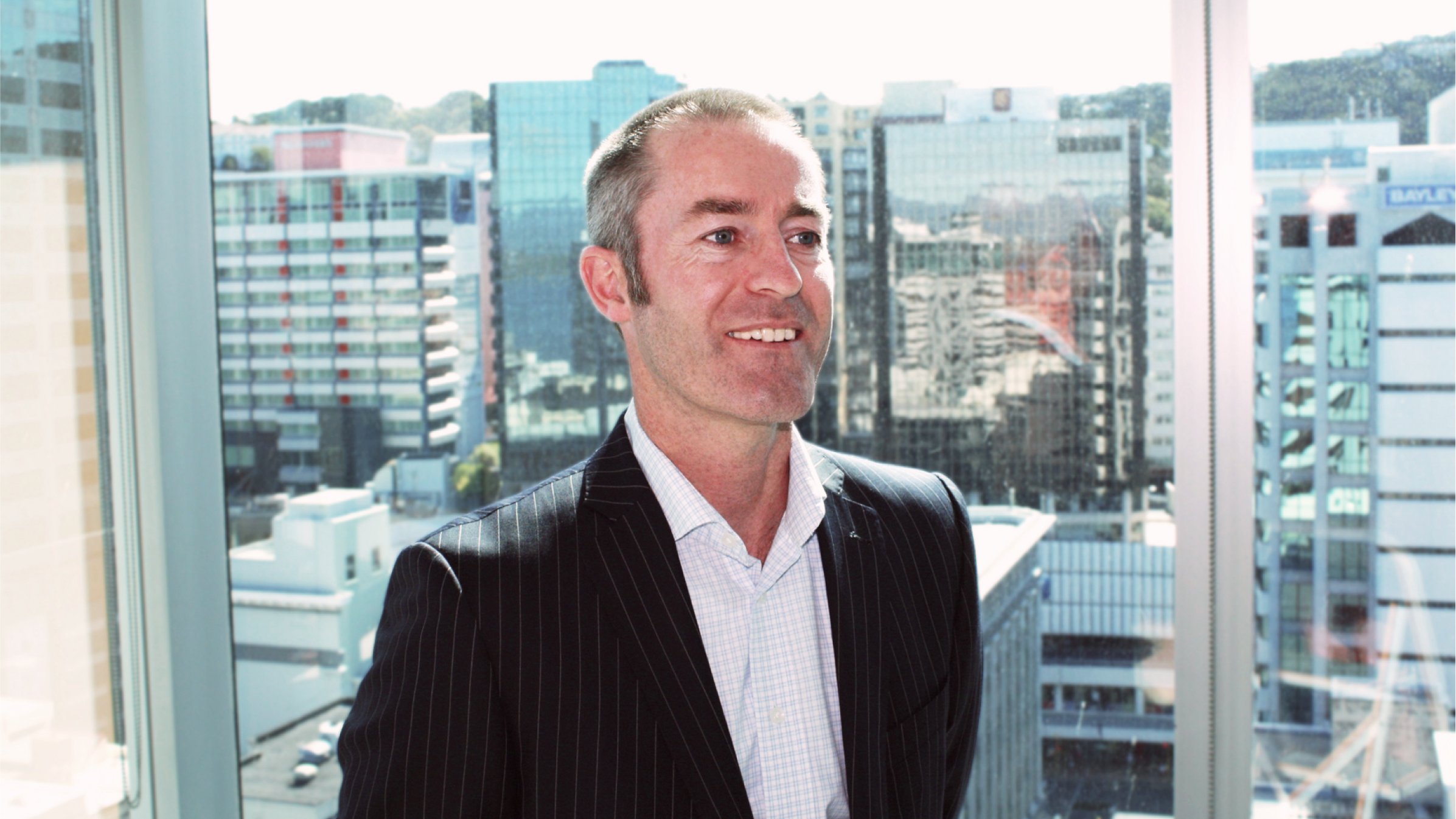 Stephen Nicholas, Partner at Deloitte Private, stands smiling by a highrise window.