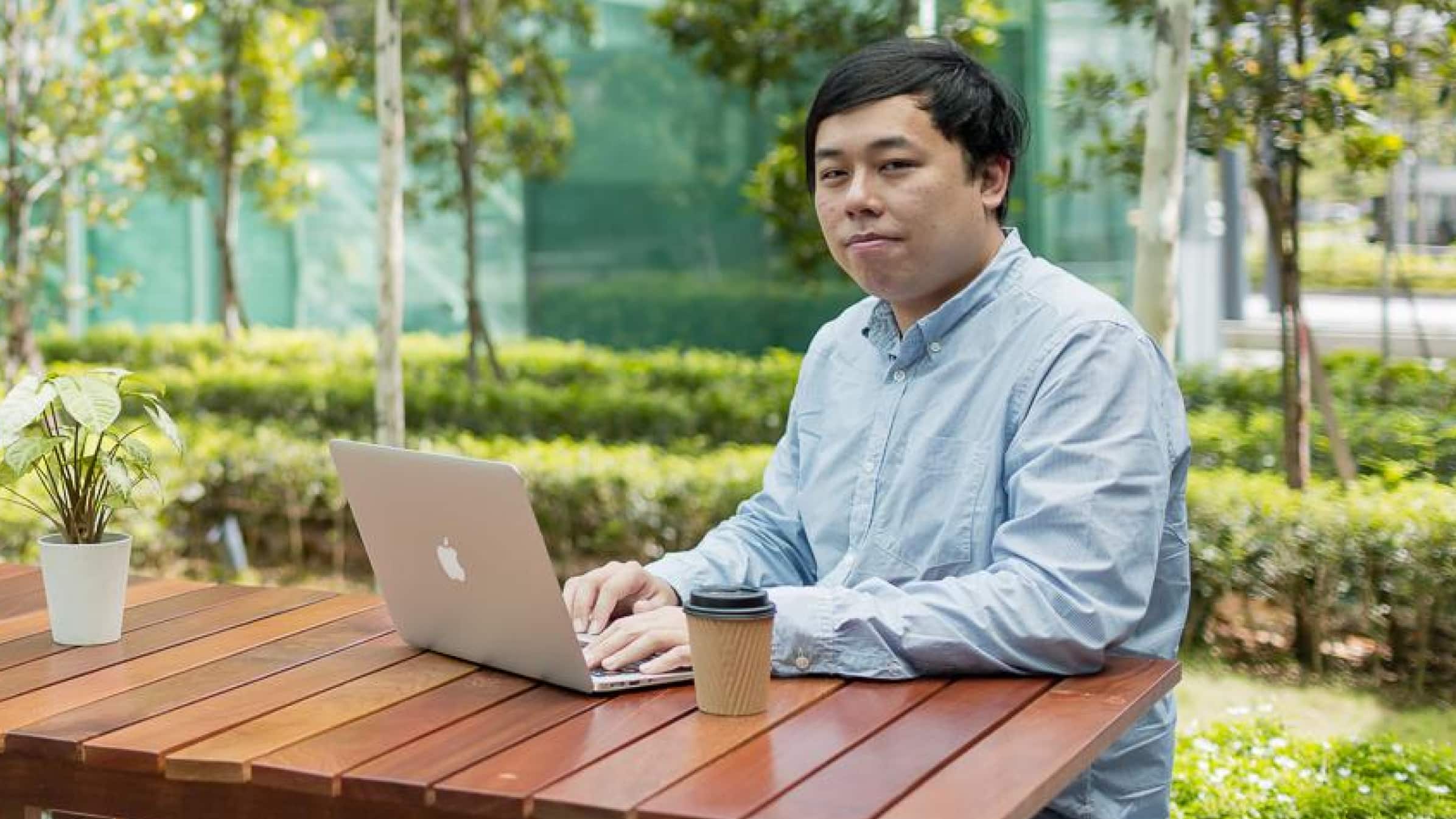 Lucas Chong from G&A Group working on a laptop computer at a table in a garden.