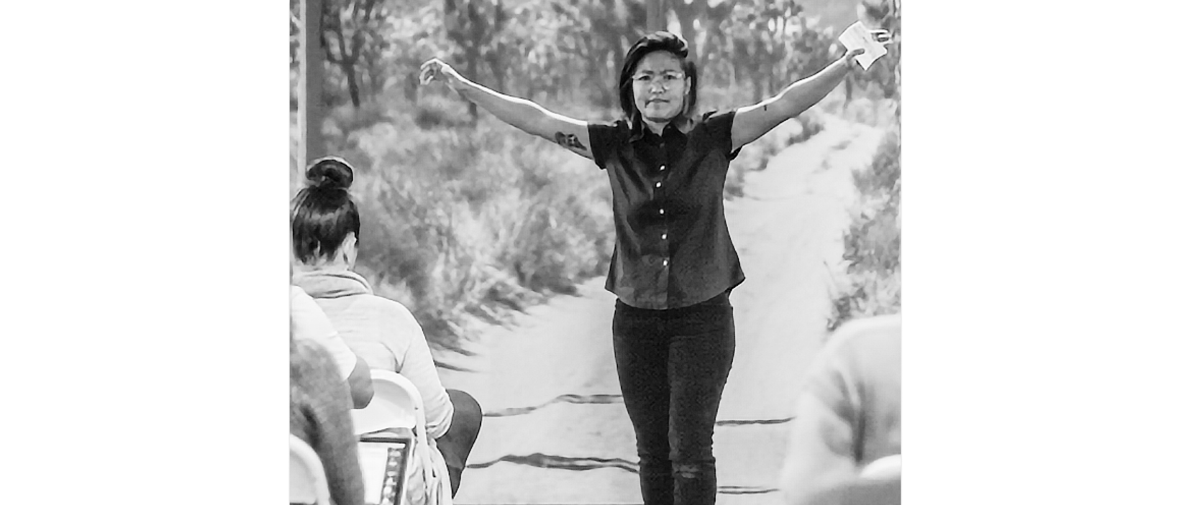 aco standing with arms expressively outstretched as she gives a talk to people seated in rows.