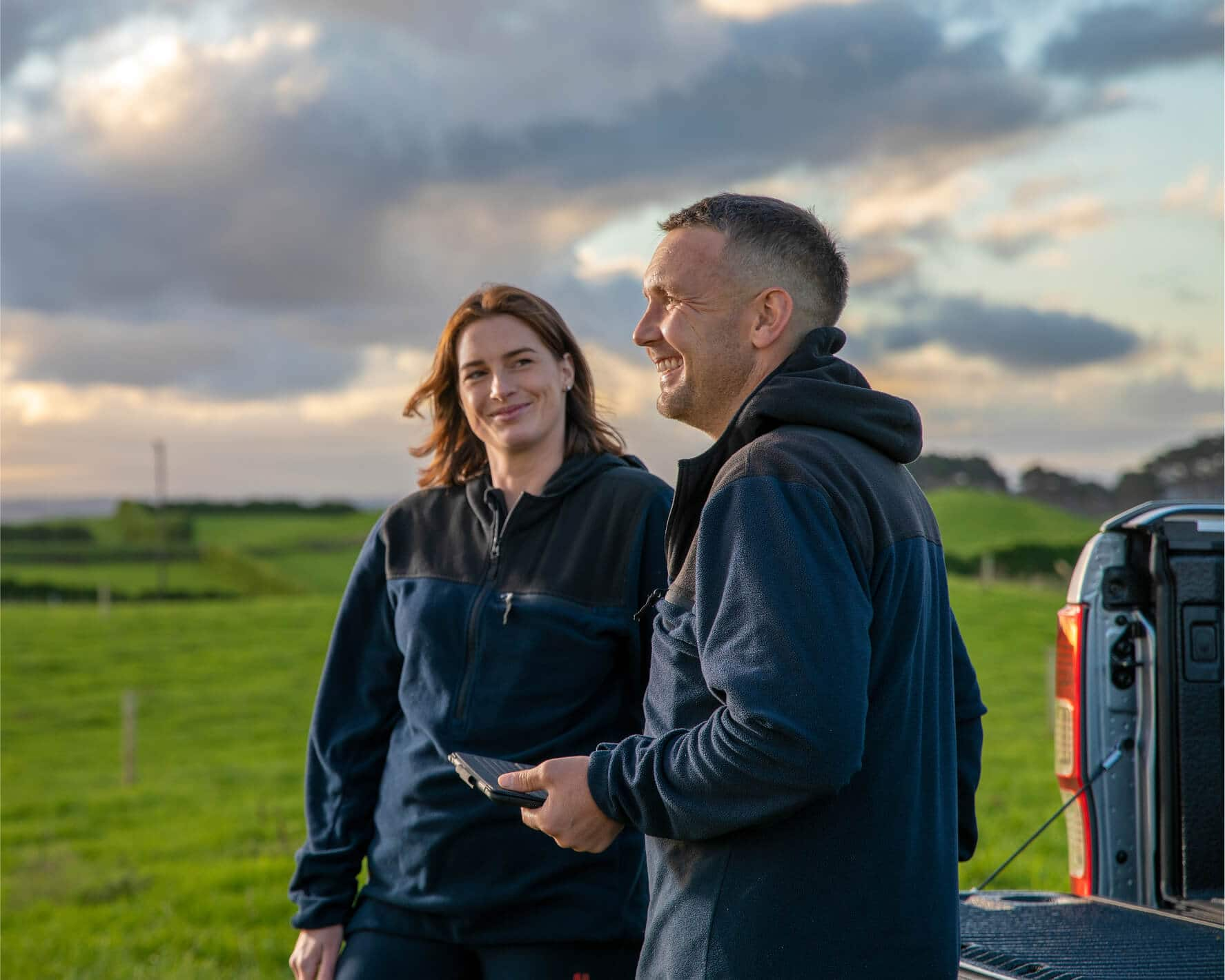 A farmer in a field with their advisor, checking figures in the agriculture accounting software on their mobile.