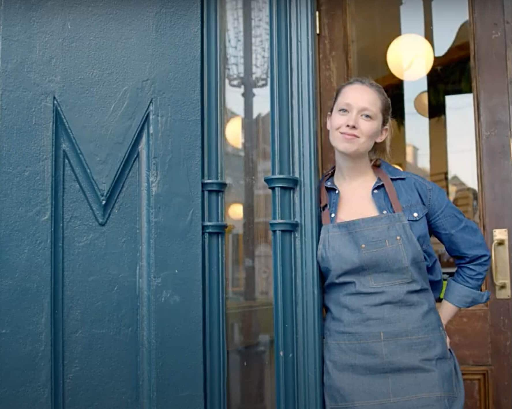 A cafe owner stands at the door looking out at the street.