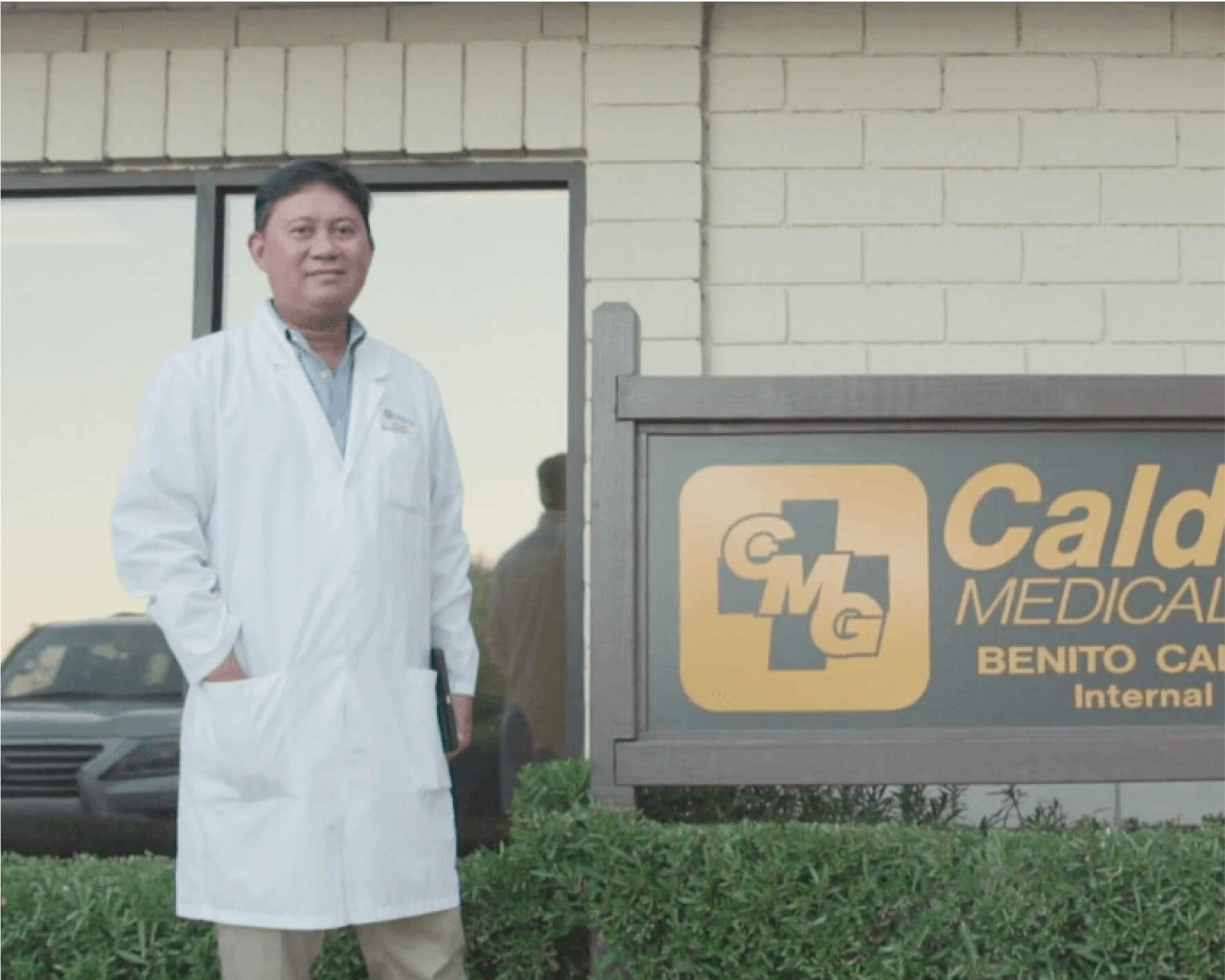 A person in a lab coat stands outside of an office building.