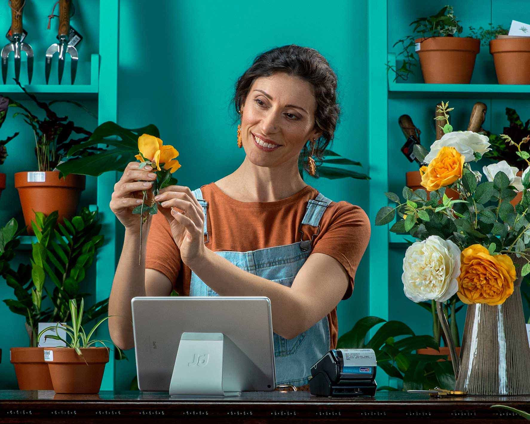 A florist prepares a bunch of flowers with Xero open on a laptop on the counter in front of them.