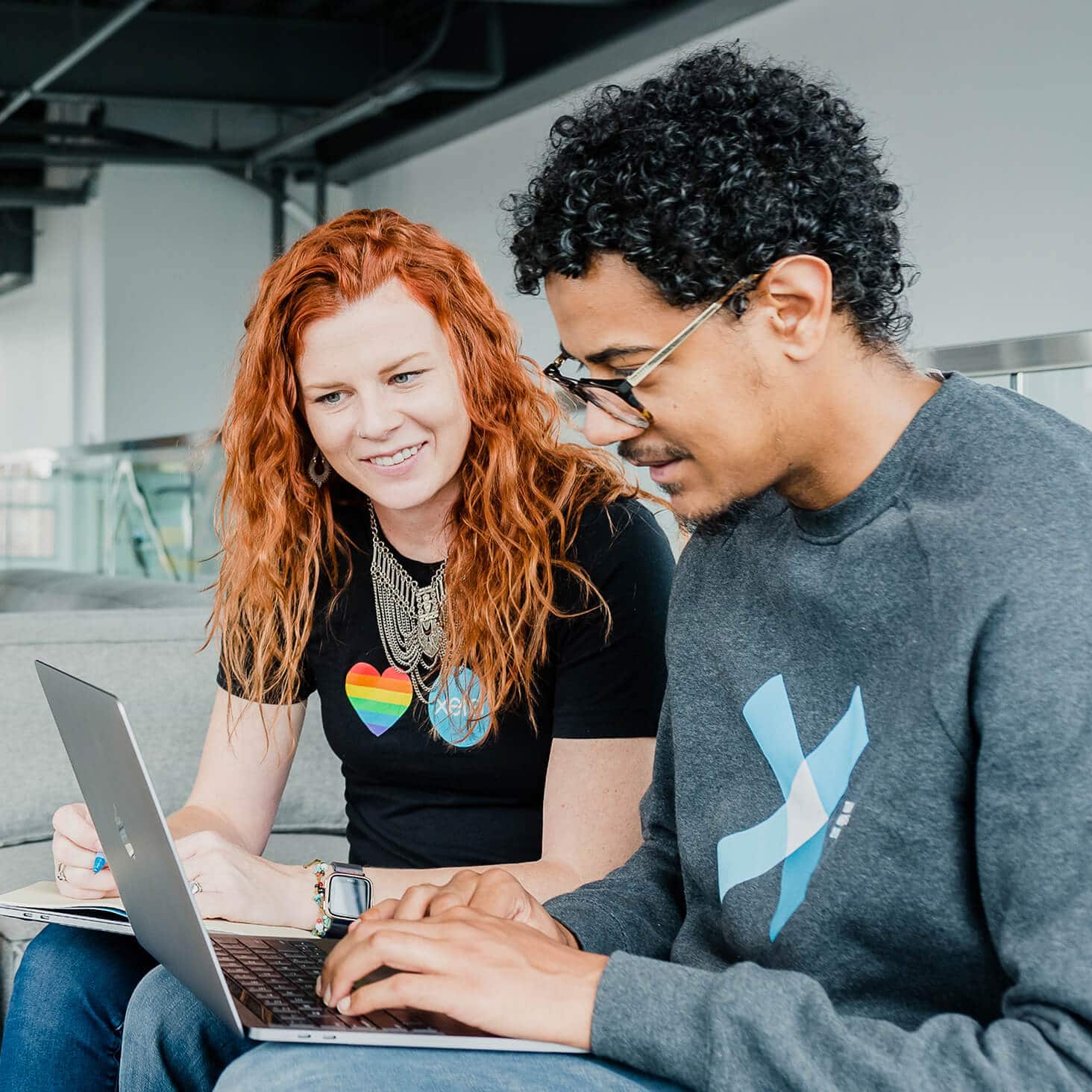 Two Xero employees, both wearing staff tee shirts, work together on a laptop