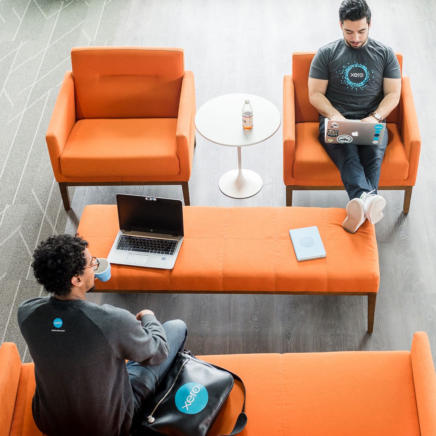Two people working on laptops on orange couches.