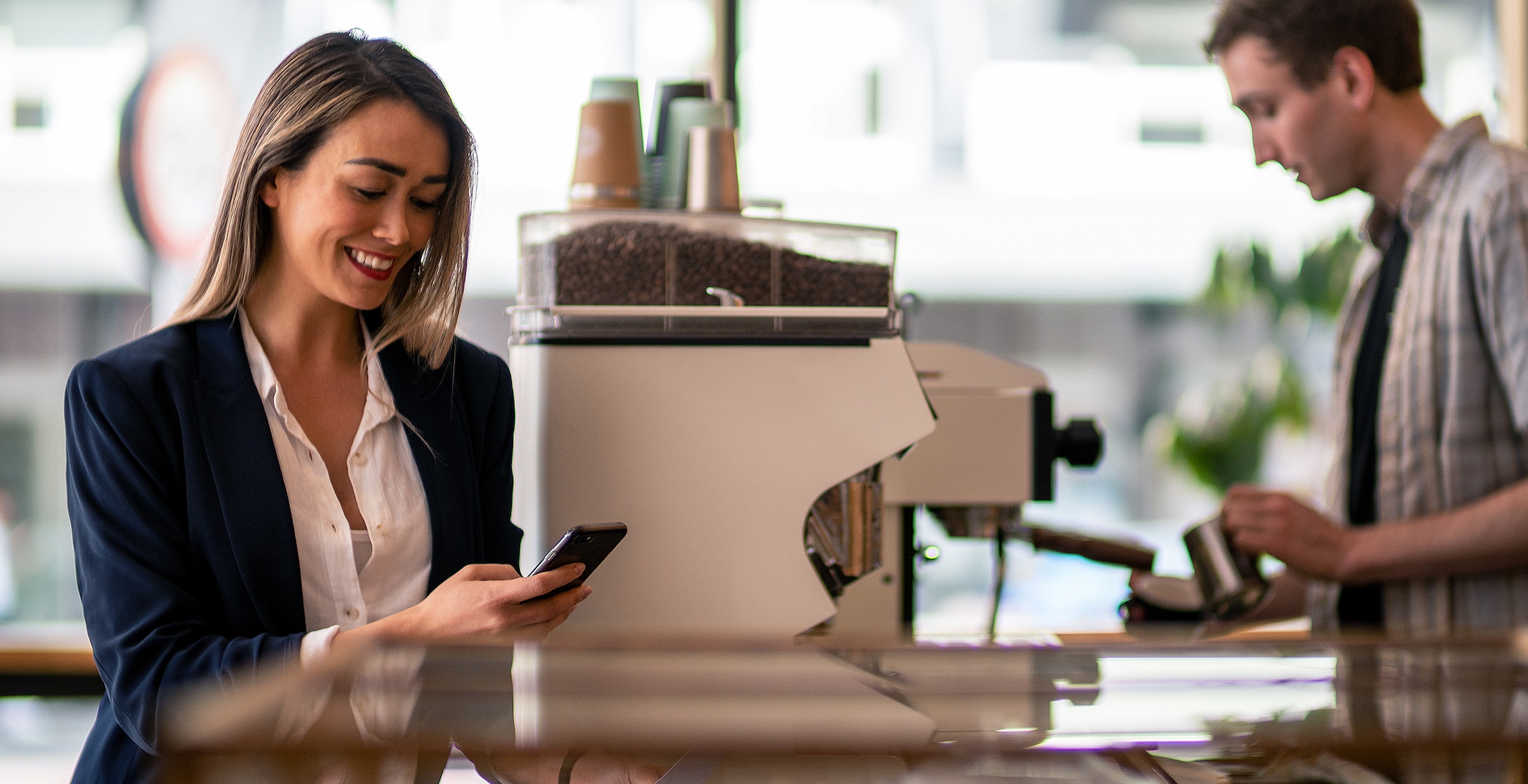 A small business owner reads about responsible data use on their phone while waiting for coffee from a barista.