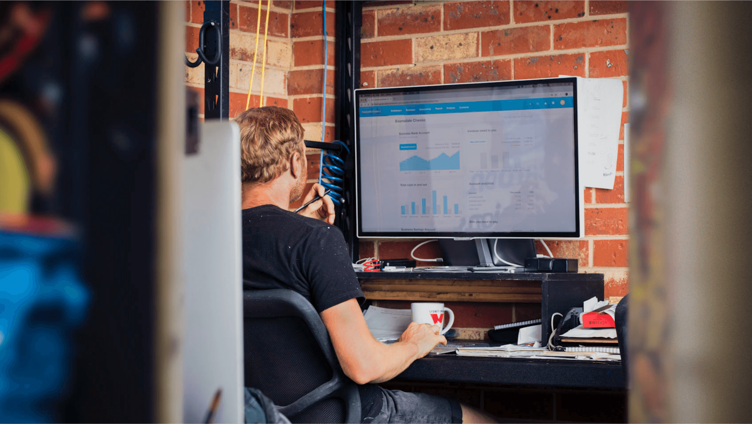 A small business owner views charts showing business data in Xero on a large computer monitor.