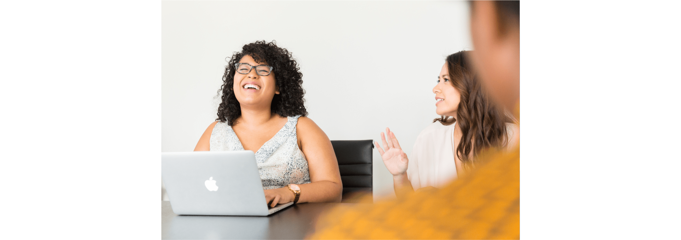 Two women share a light-hearted moment while working at a laptop.