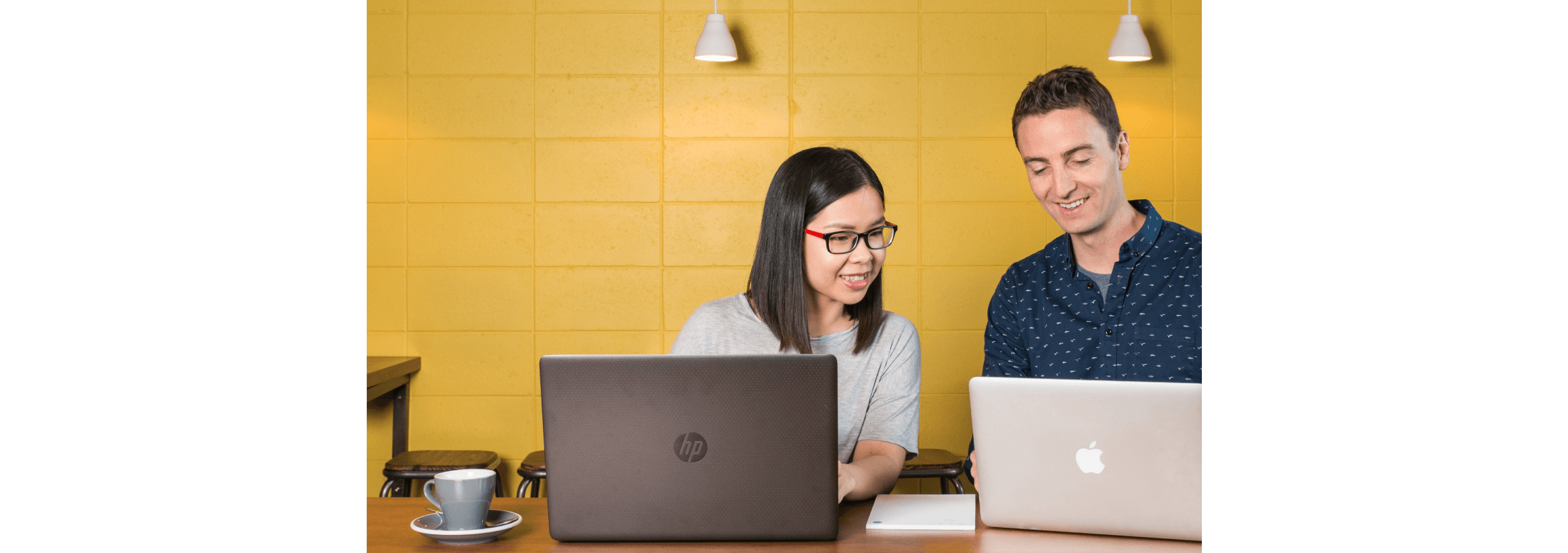 Two people working together at their laptops in an office kitchen.  