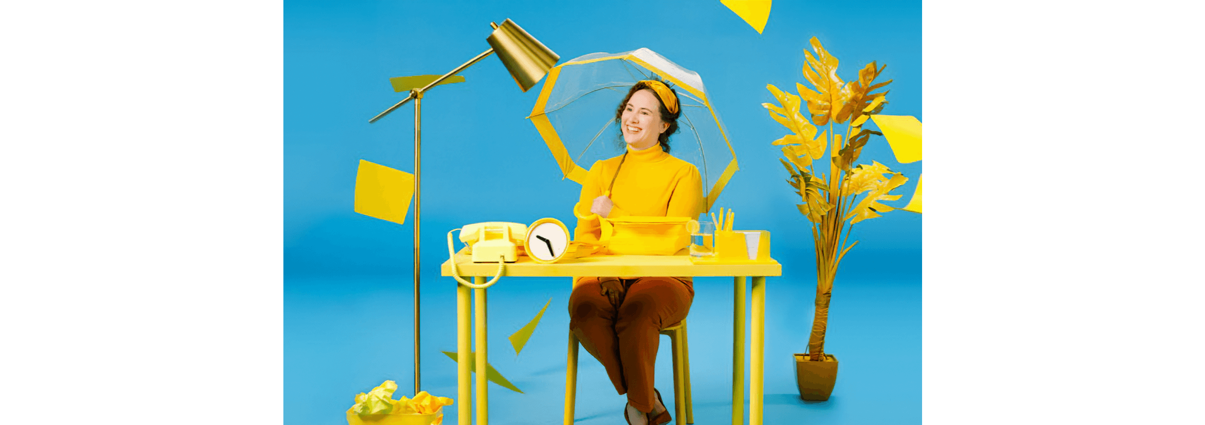 A person sitting at a desk holding an umbrella over their head.