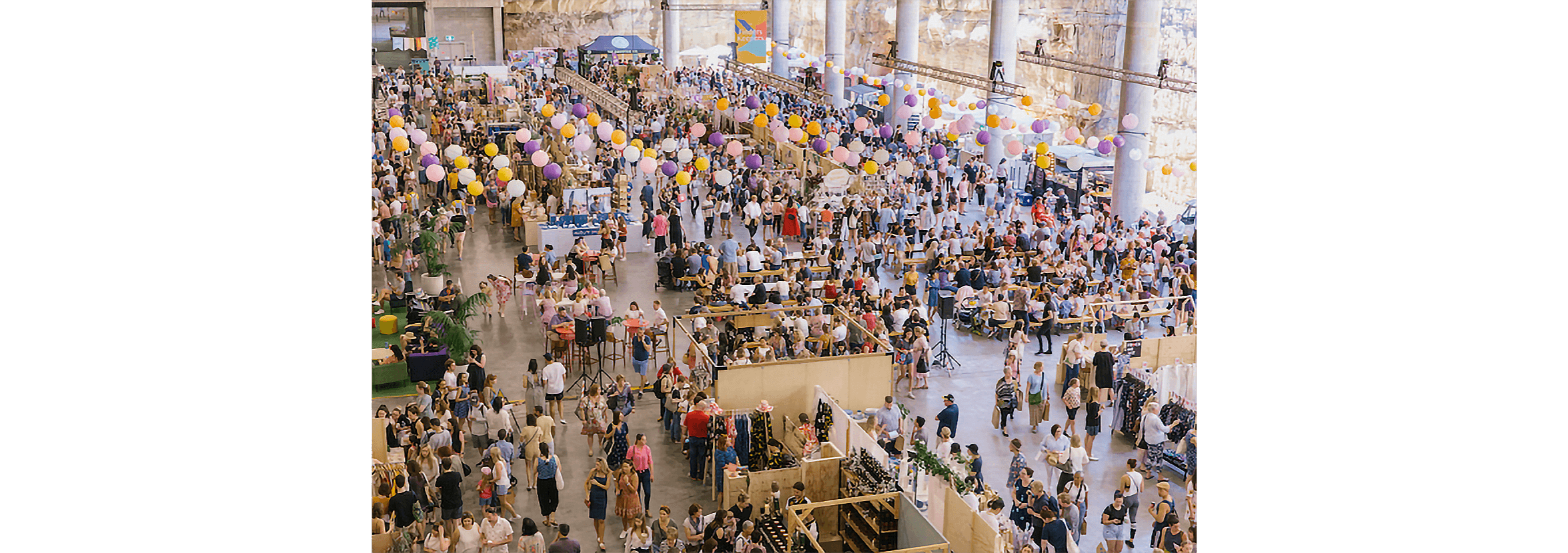 A large crowd of people peruse the stalls at an indoor charity fair.