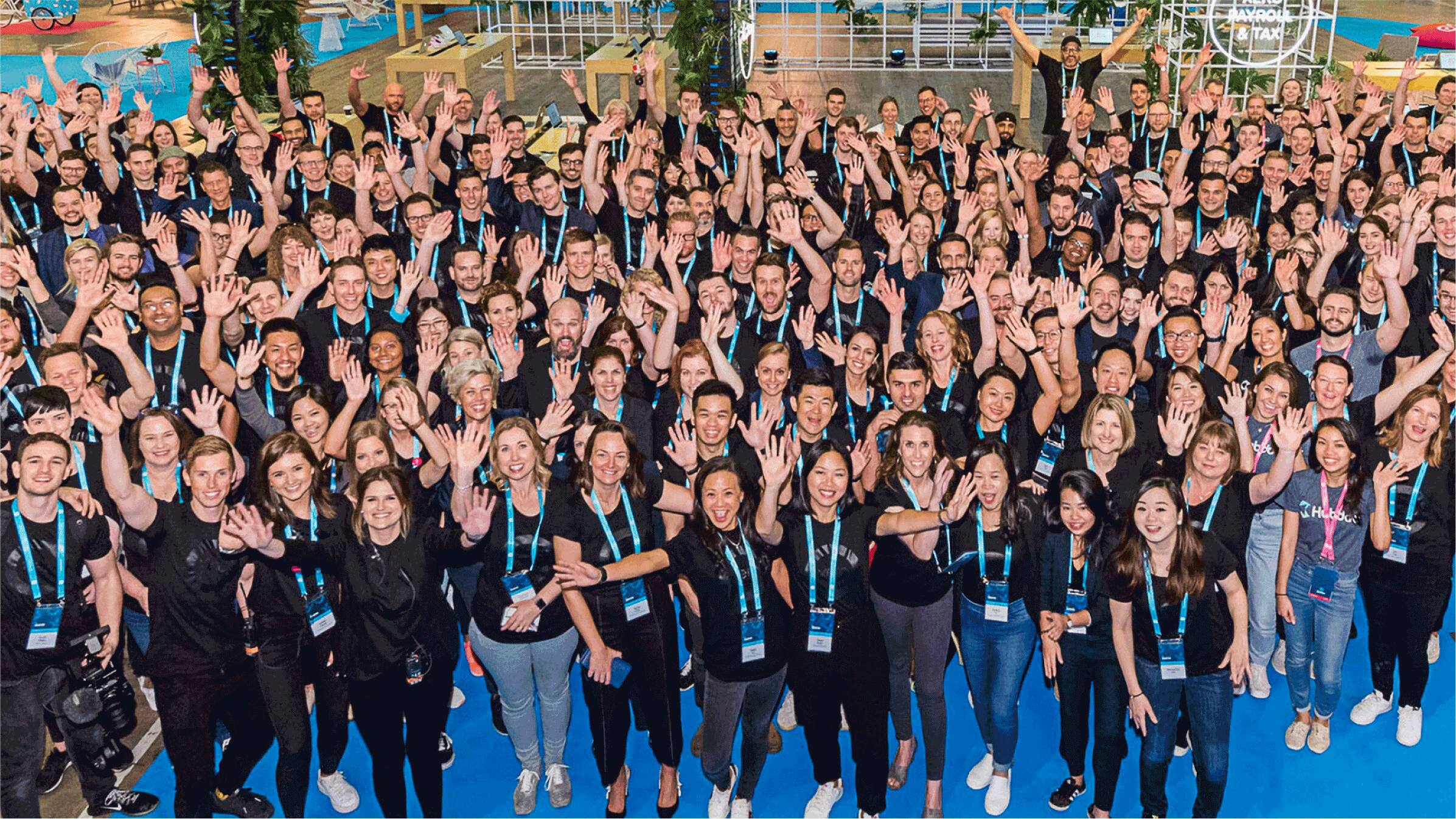 A large crowd of Xero staff members raising their arms in the air.