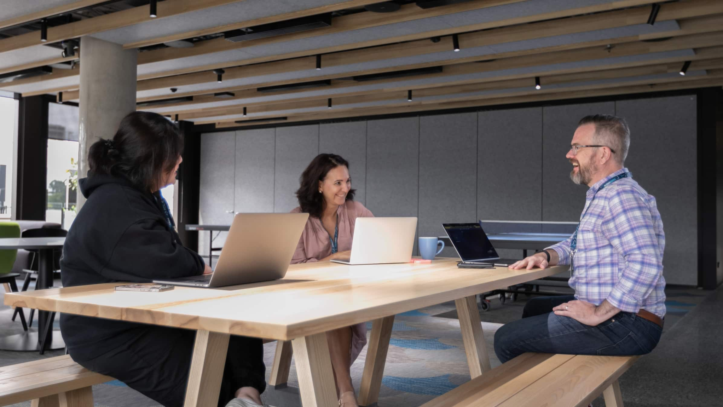  Three Xero employees share a laugh while meeting in an informal work space, laptops open in front of them.