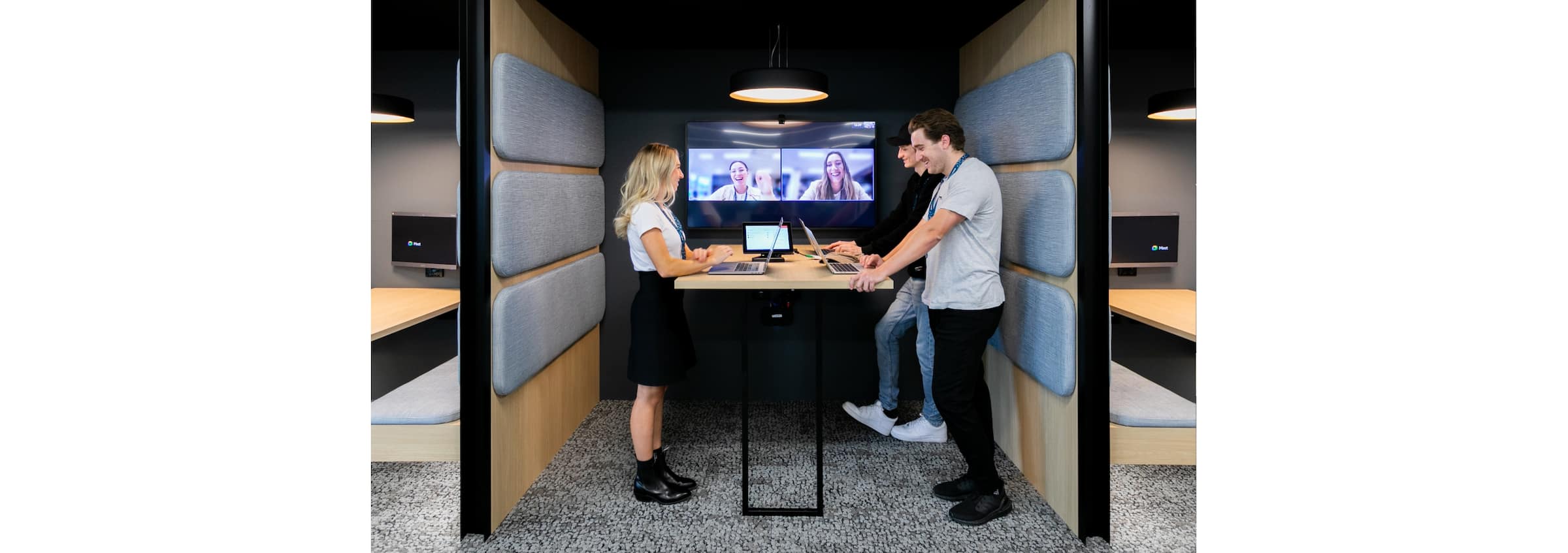 Three of the Xero team stand at a table in a meeting space, in an online meeting with two other people on the screen.