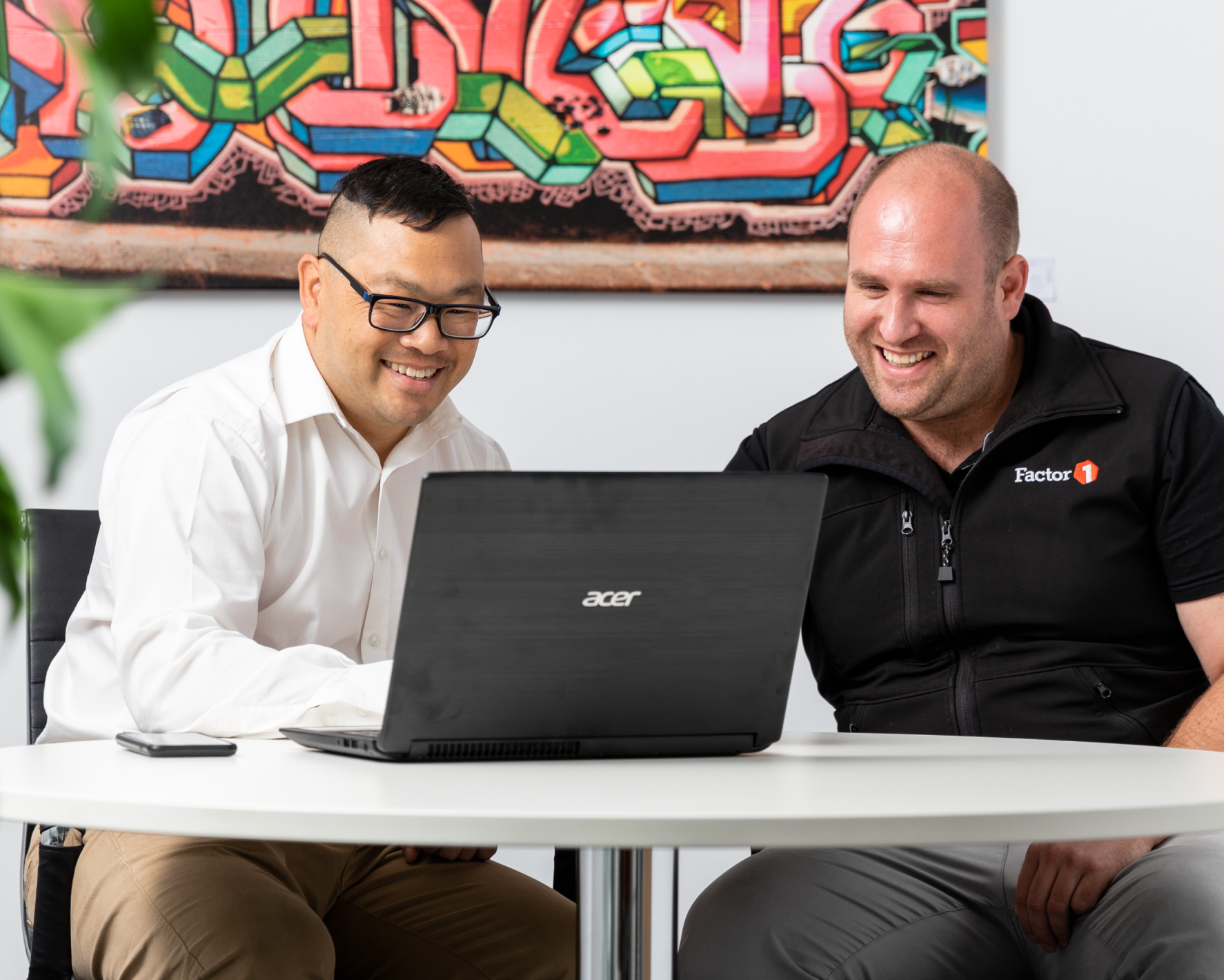 Two men sitting at a table and smiling at a laptop