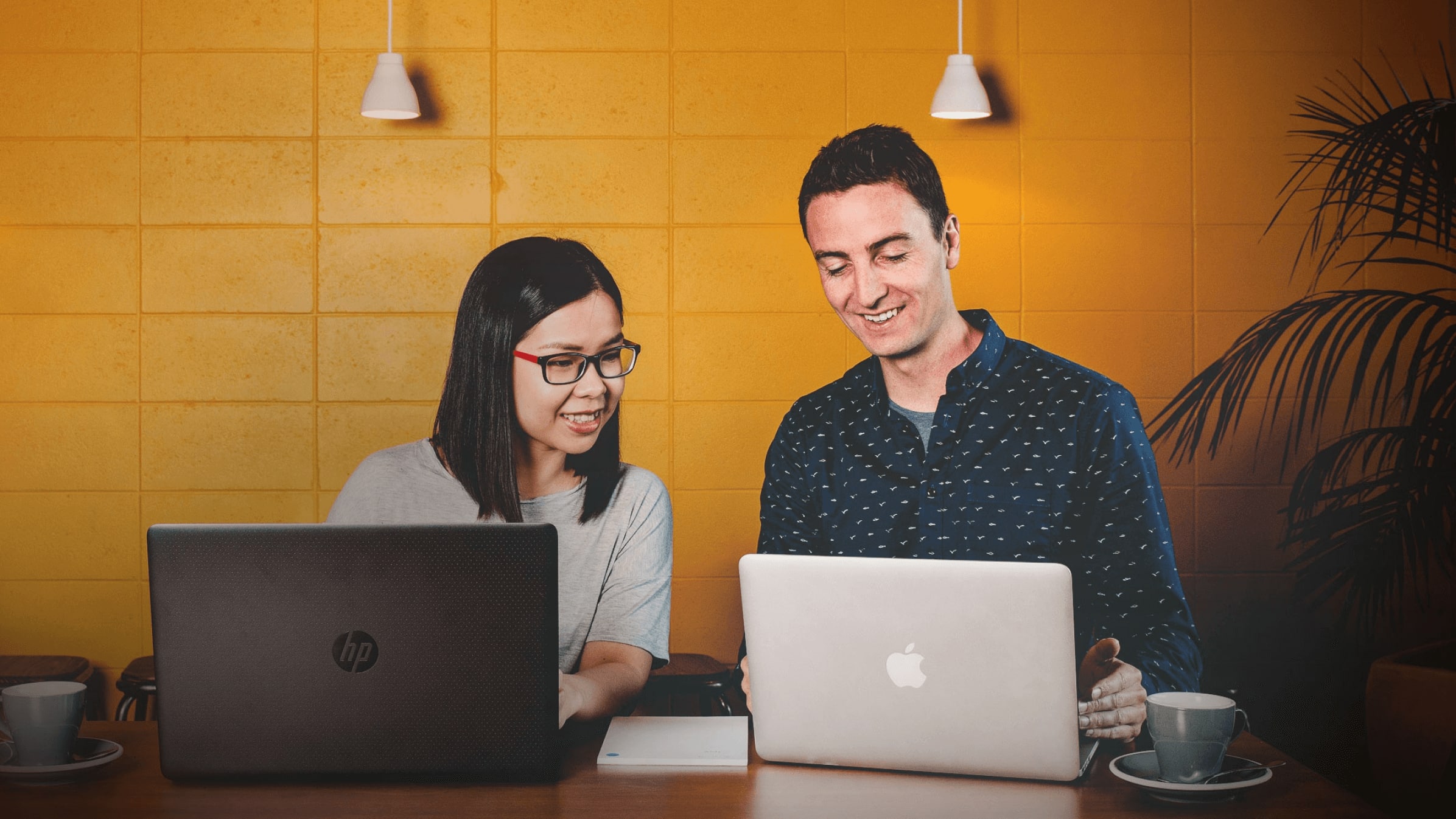 Two business owners sitting next to each other with a cup of coffee reading from their laptops.