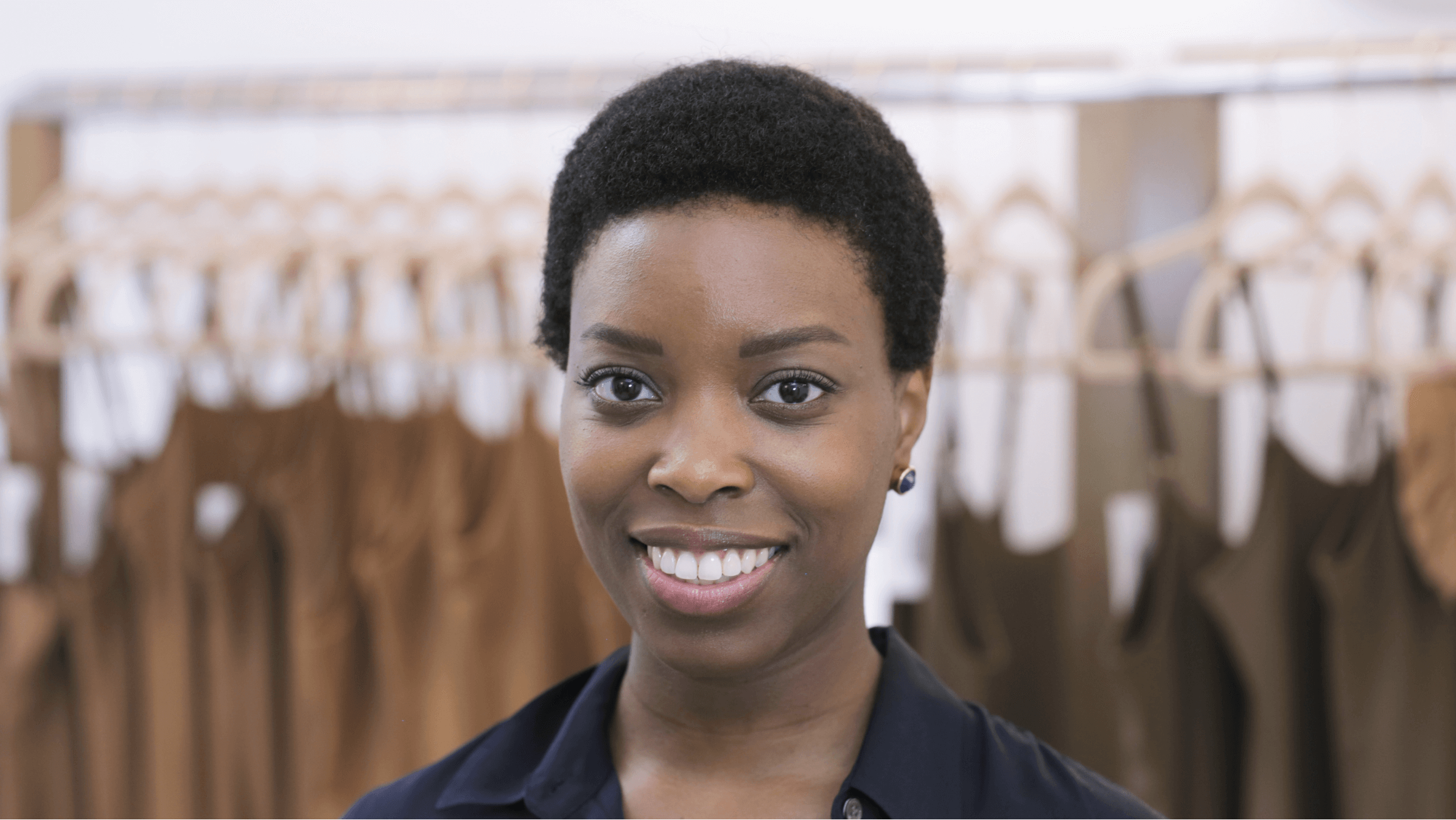 Ade Hassan, owner of fashion brand Nubian Skin, stands in front of a row of slips on hangers.