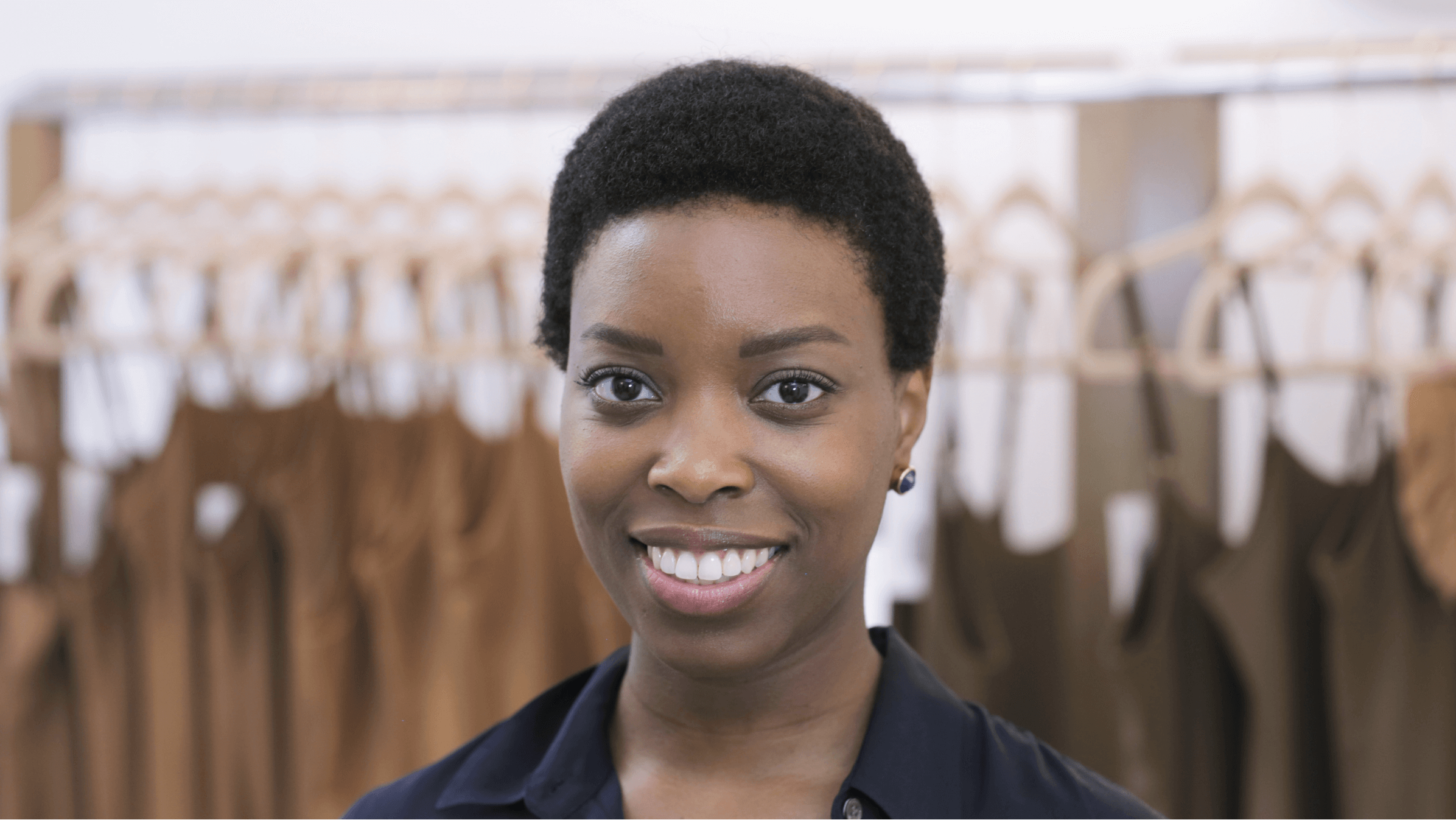 Ade Hassan, owner of fashion brand Nubian Skin, stands in front of a row of slips on hangers. 