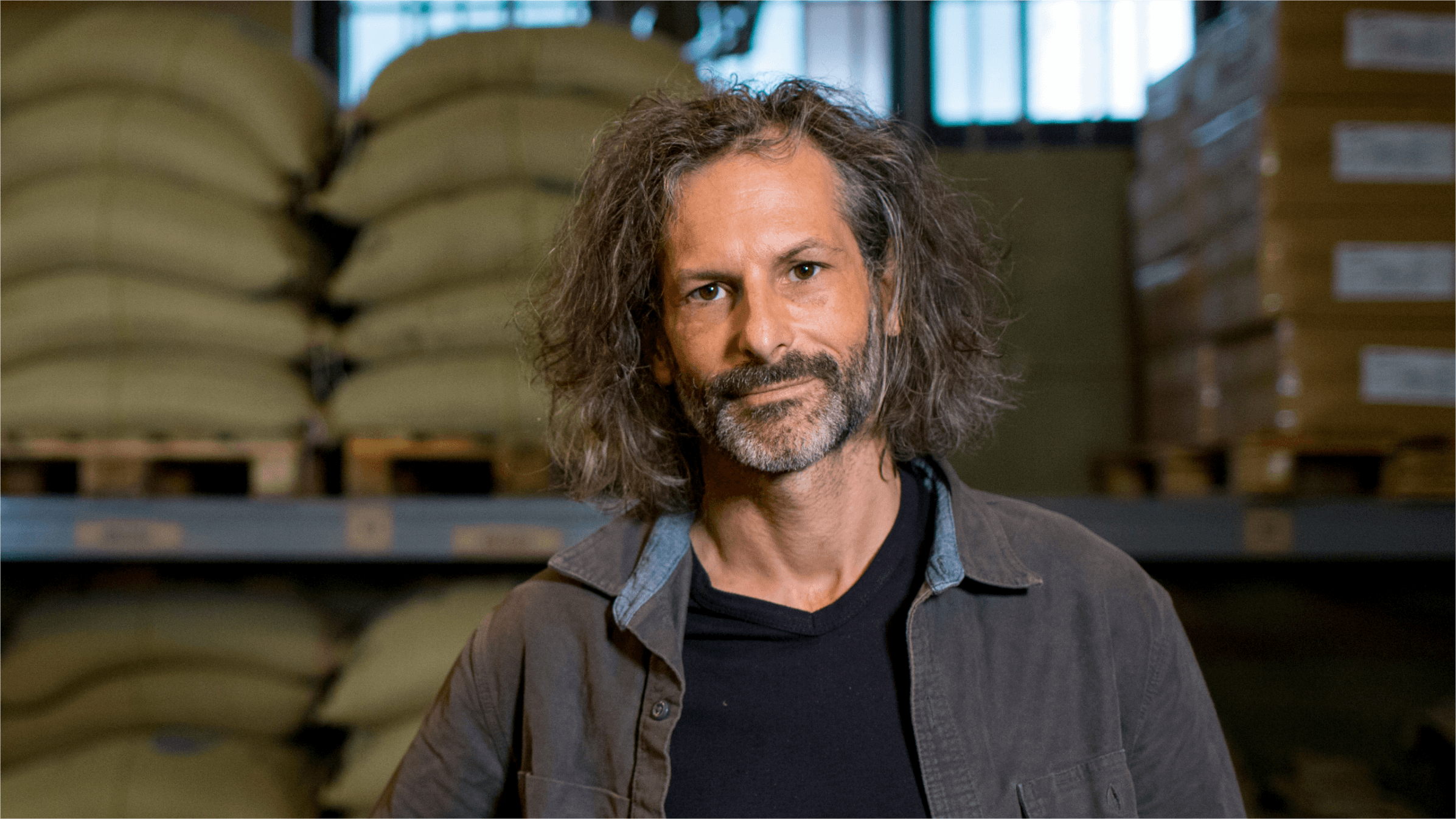 David stands in the storeroom of Truth Coffee in front of sacks of coffee beans.