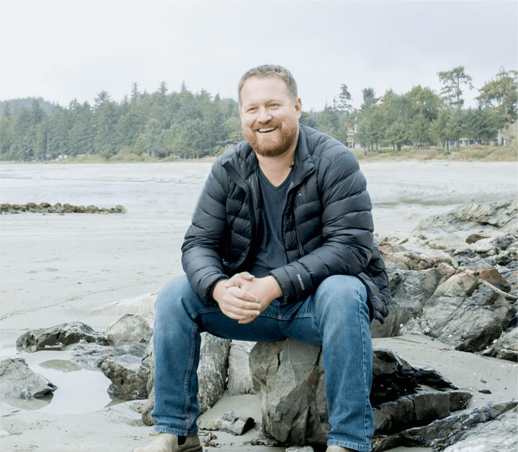 Chad Davis, partner and co-founder of LiveCA, sitting on rocks by the sea.
