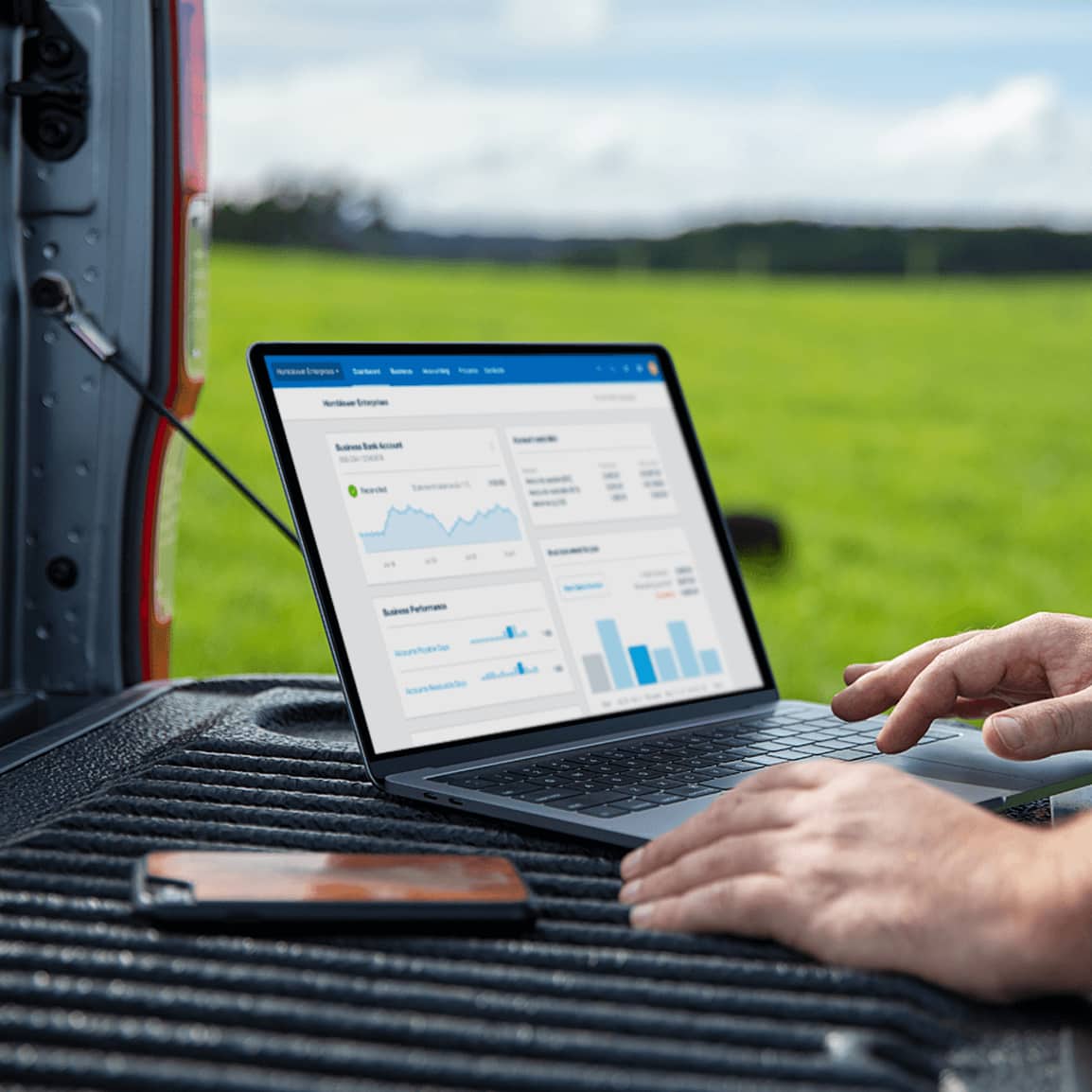 A farmer checking Xero for farming financials on a notebook computer in the field, using the bed of a ute as their desk.