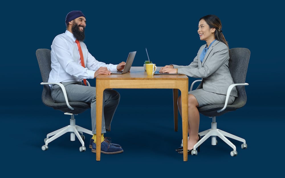 Two partners sitting at a desk smiling at each other.