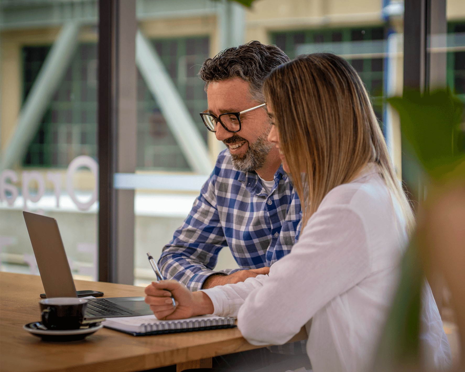 A business owner and employee working together at a table, using Xero’s employee management add-ons on a laptop computer. 