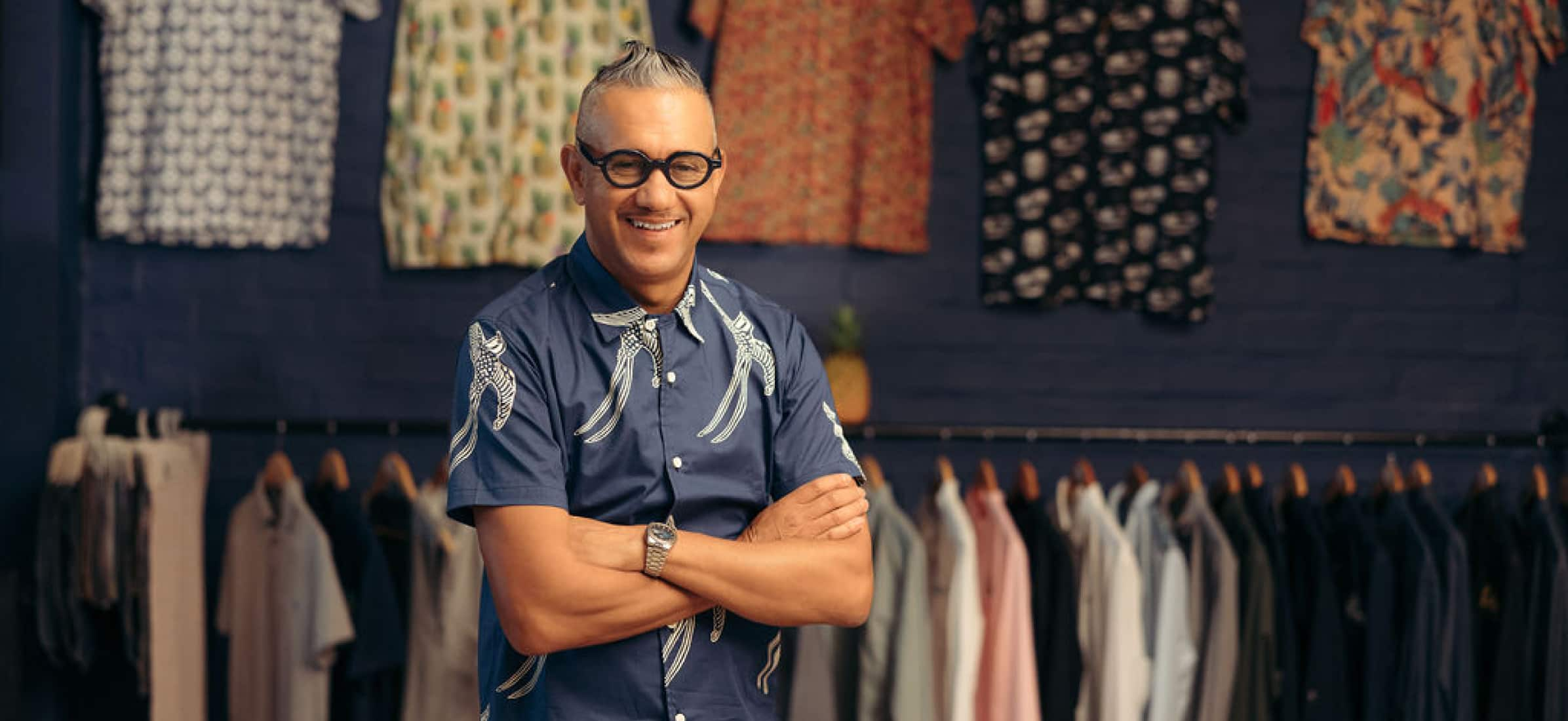 Upper body photo of Adrian Heneke standing in front of patterned shirts.