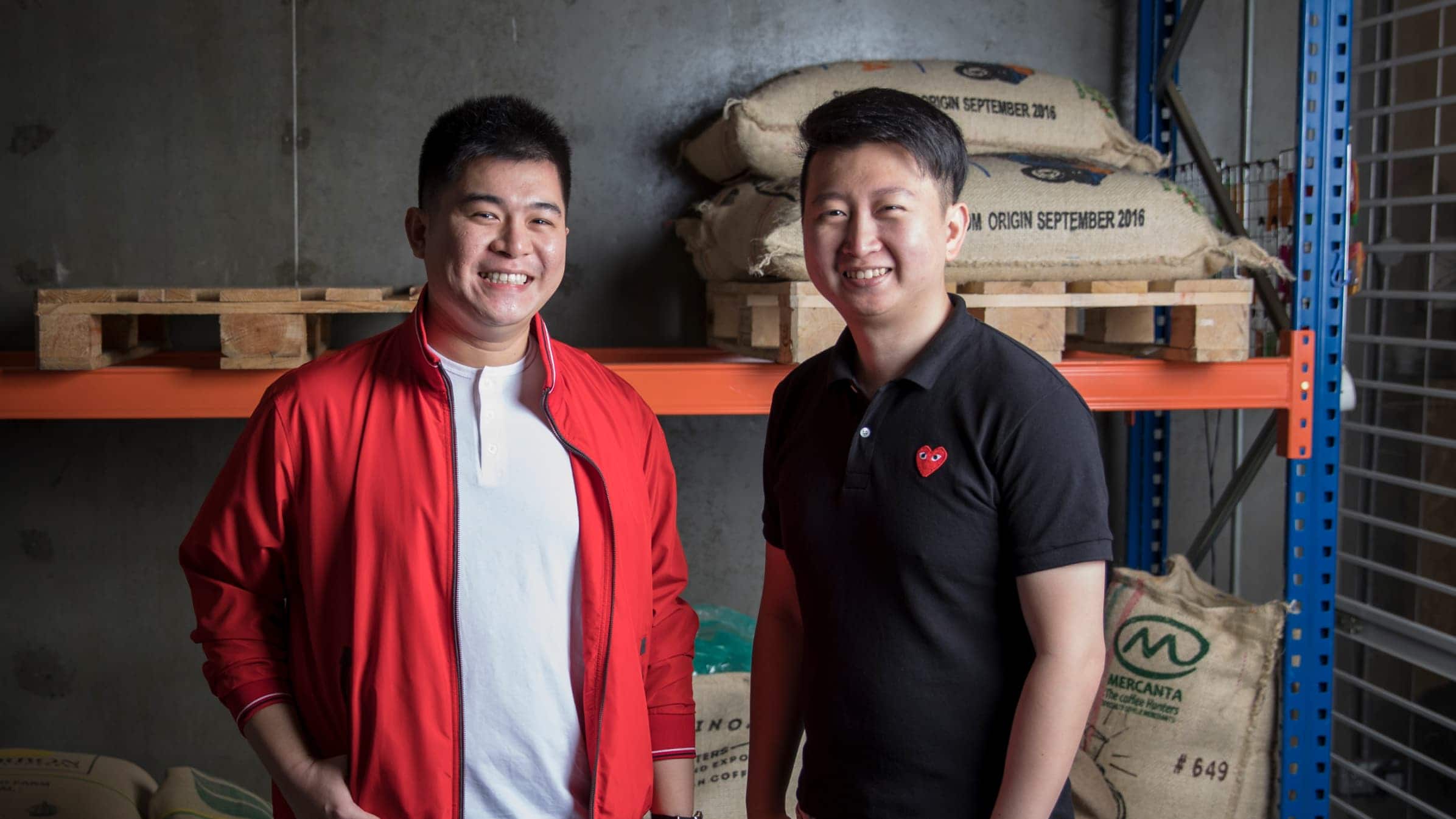 Keyis Ng and Eugene Chen standing in their coffee warehouse smiling to camera.