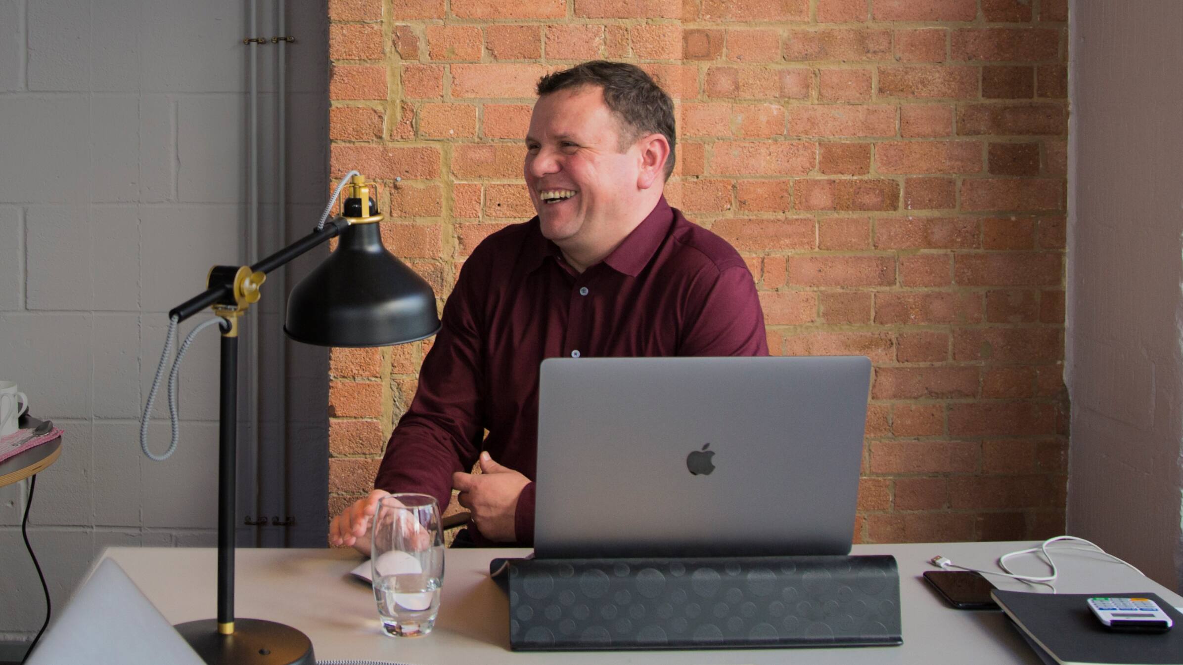 Steven Anderson, founder of creative agency Future Kings, laughing as they sit behind a laptop at their desk.