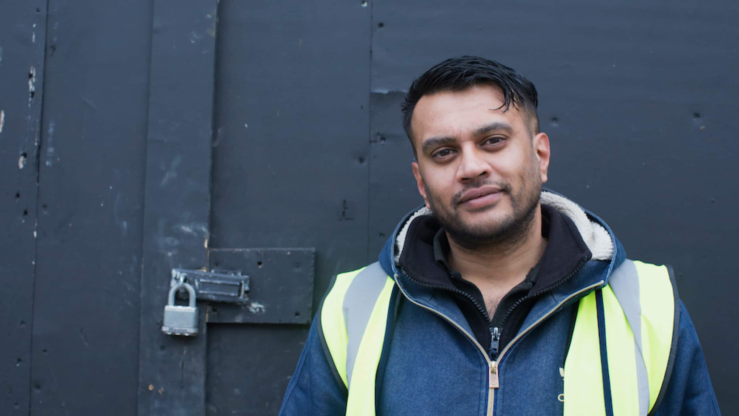 Hitesh Kanbi, founder of construction company IKPE Ltd, standing in front of a warehouse door wearing a high-vis vest.