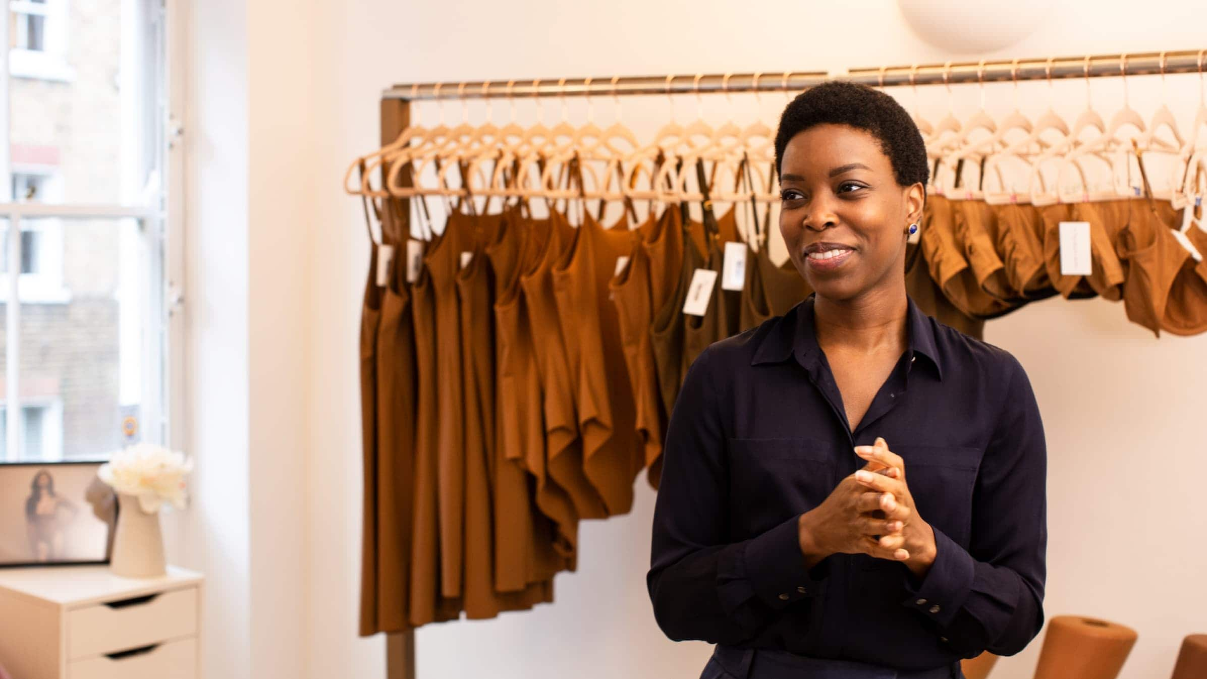 Ade Hassan, founder of fashion brand Nubian Skin, standing in front of a line of clothes.