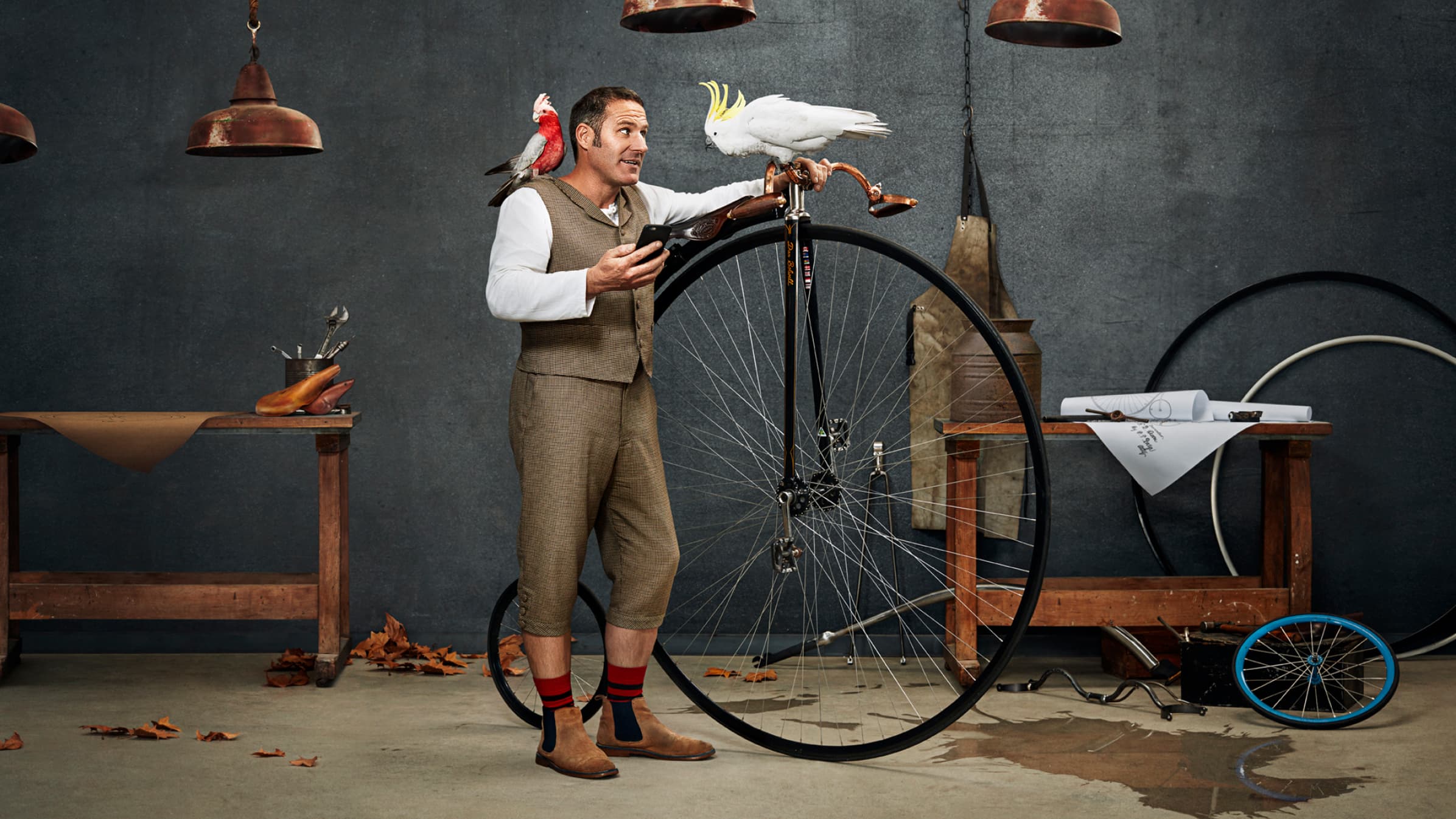 Dan Blowell stands with his penny-farthing bicycle, where a cockatoo bird randomly sits on the handles.