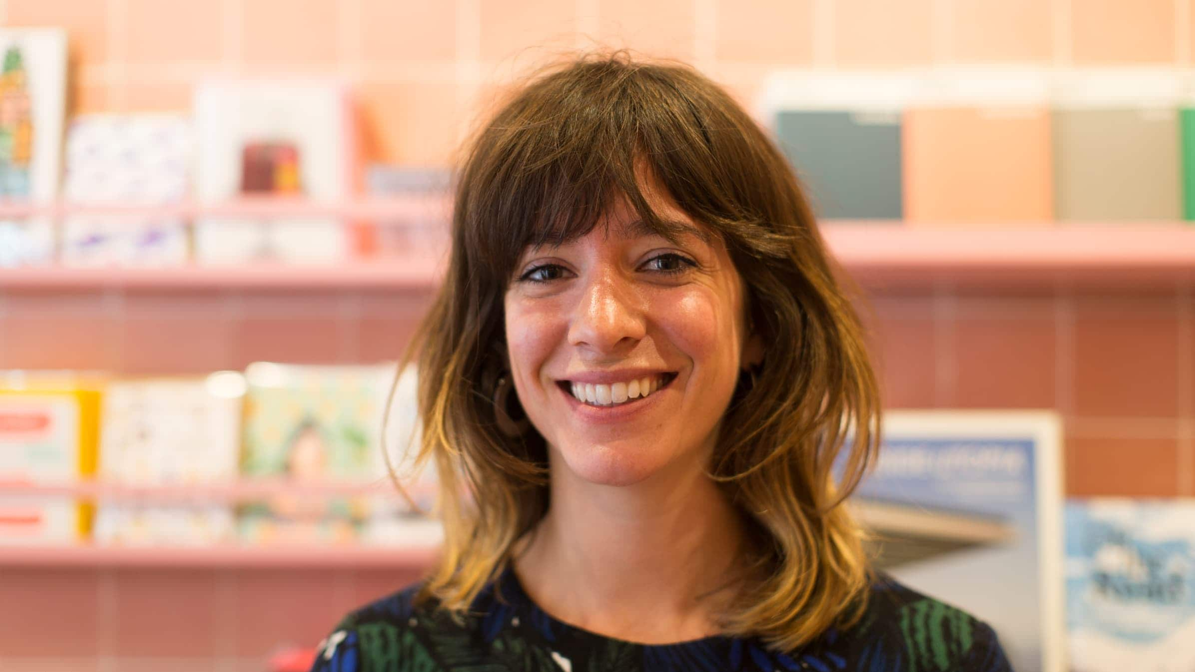 Sidonie Warren, founder of Papersmiths, standing in her store in front of a card rack smiling at the camera.