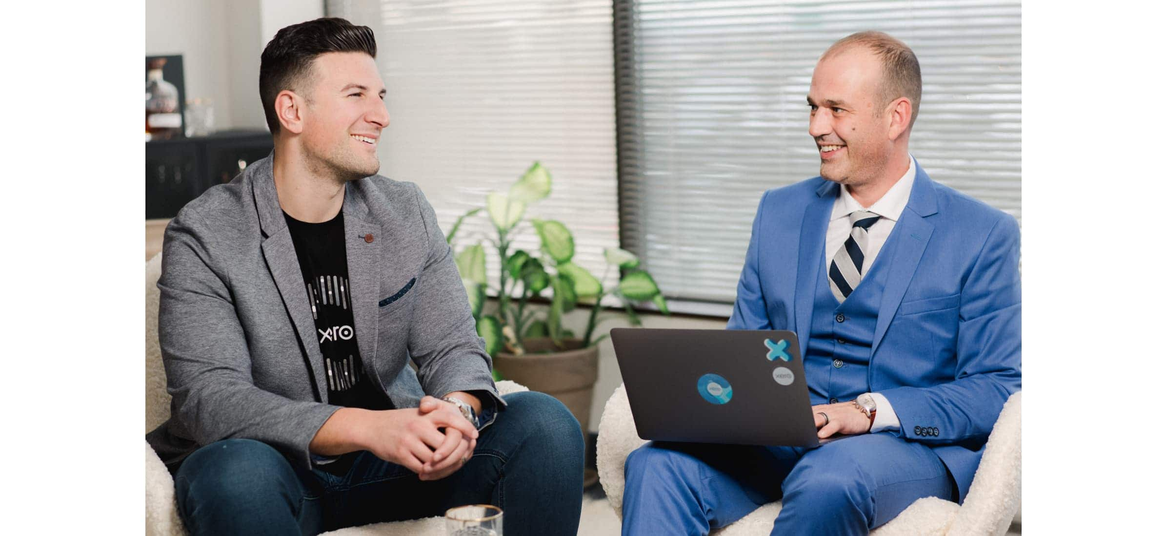 Marc laughs with a colleague while working on a computer, as they sit in armchairs in an office.