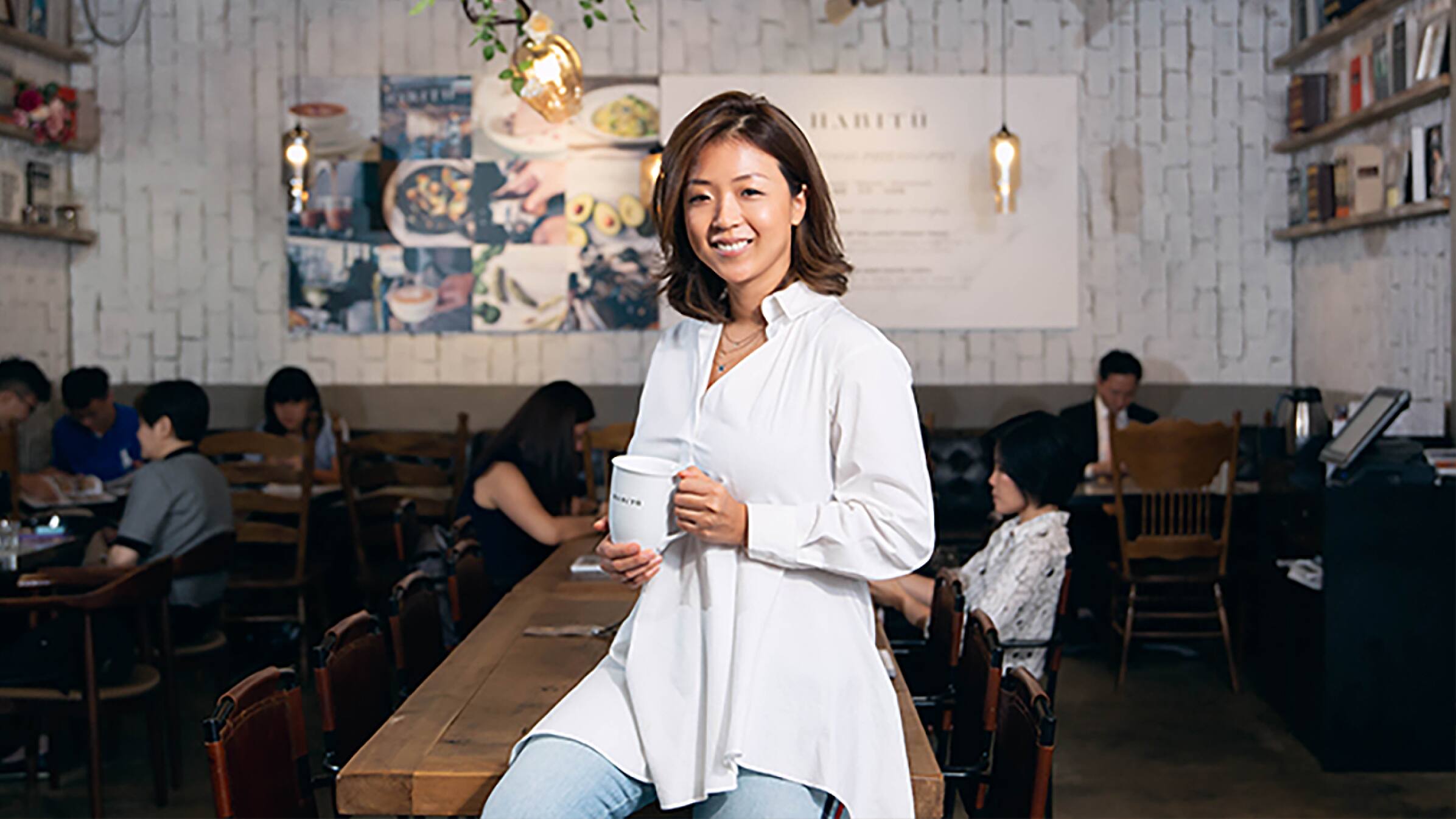 Jennifer Liu leaning against a table holding a cup of coffee inside Habitū Cafe.