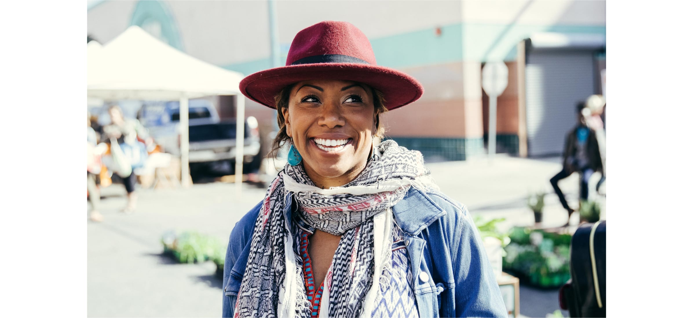 A smiling person wearing a fedora hat and colourful scarf.