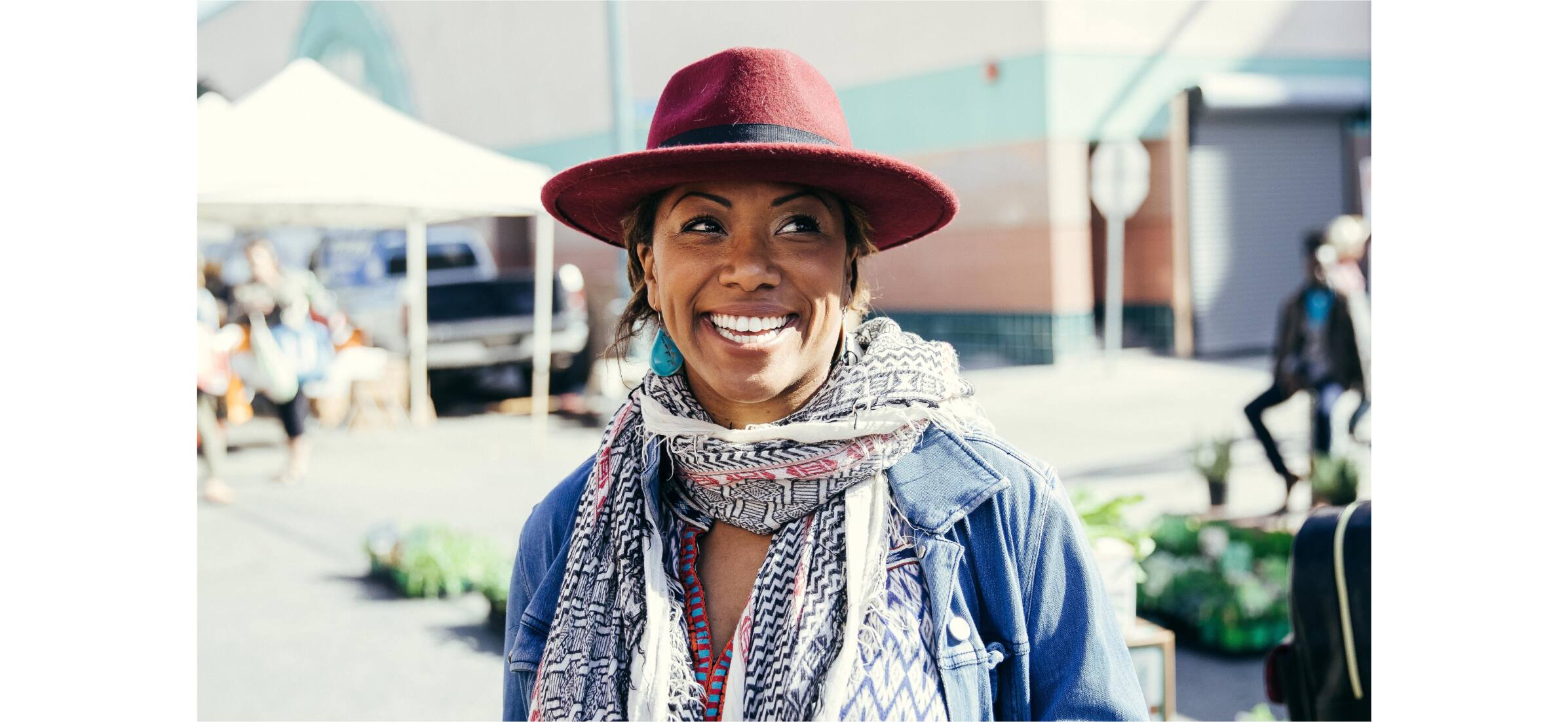 A smiling person wearing a fedora hat and colourful scarf.