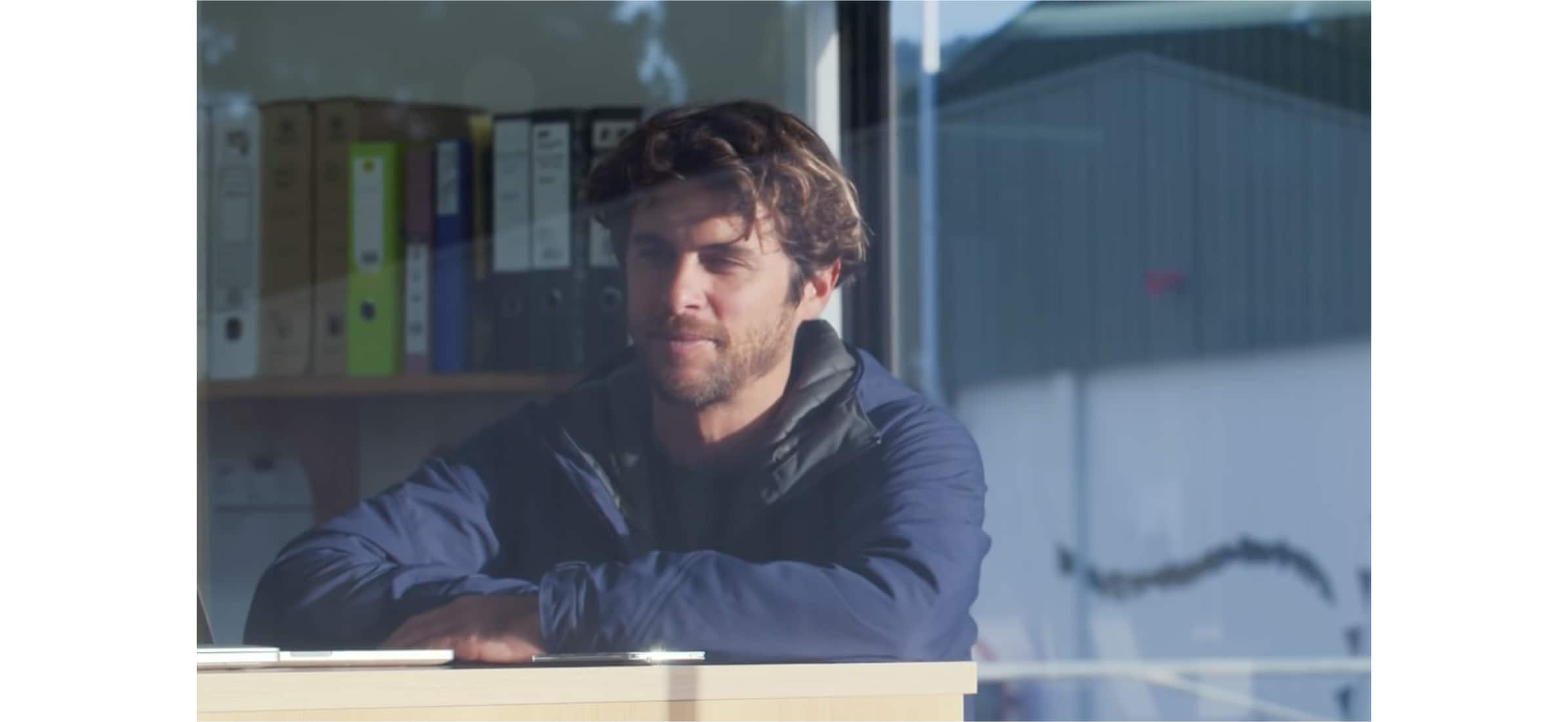 A fisherperson looking outside their office from behind a window. Files sit on a shelf behind them.