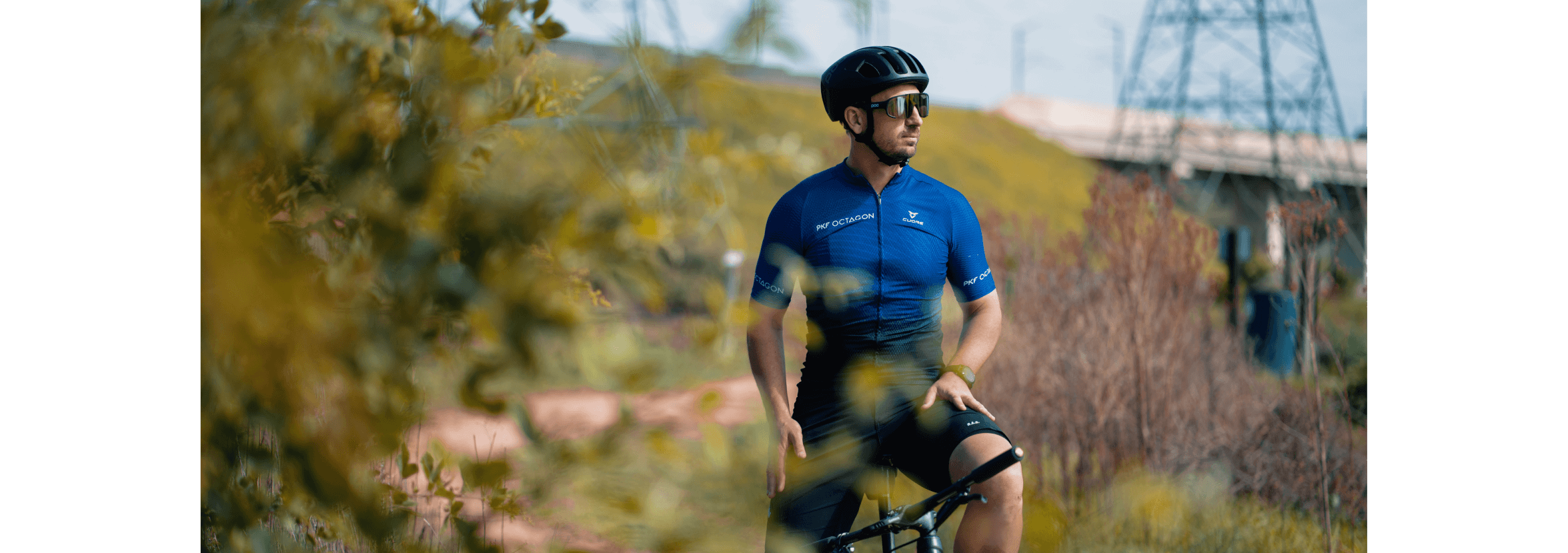 Waldek Wasowicz outside on a mountain bike, a gentle hill and a large transformer in the background.