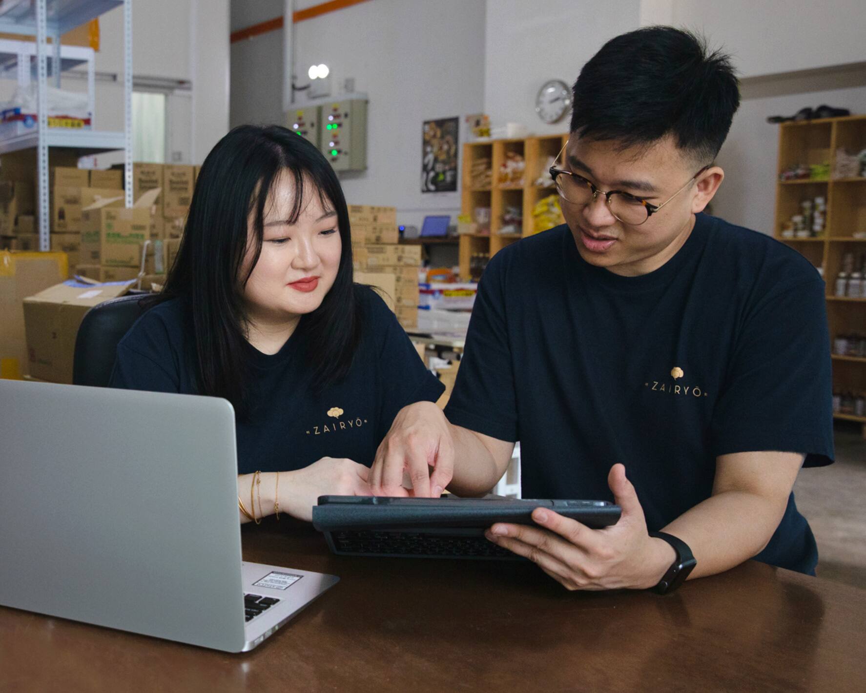 Image of the founders of ‘Zairyo’, a customer of Xero (from right to left) where two people are seated in front of a laptop and are both consulting a tablet.