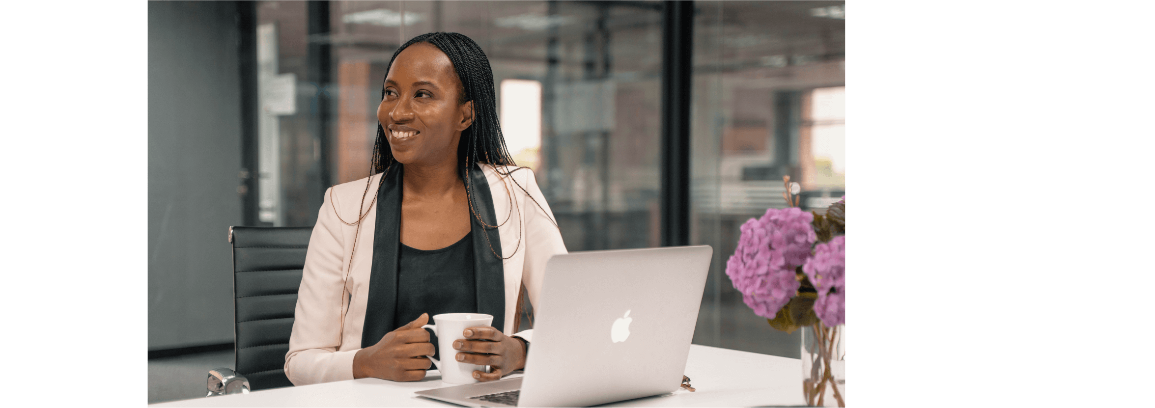 Nkhesani Kapena smiles with a cup of tea in her hands, an open laptop on the table in front of her. 