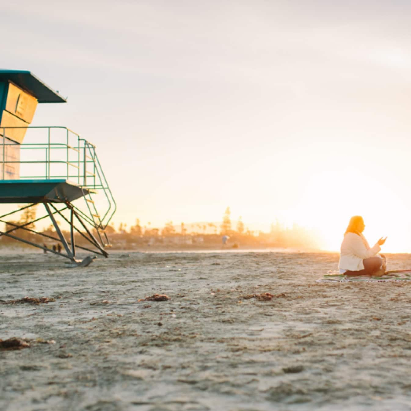 Una persona sentada en una playa durante la puesta de sol.