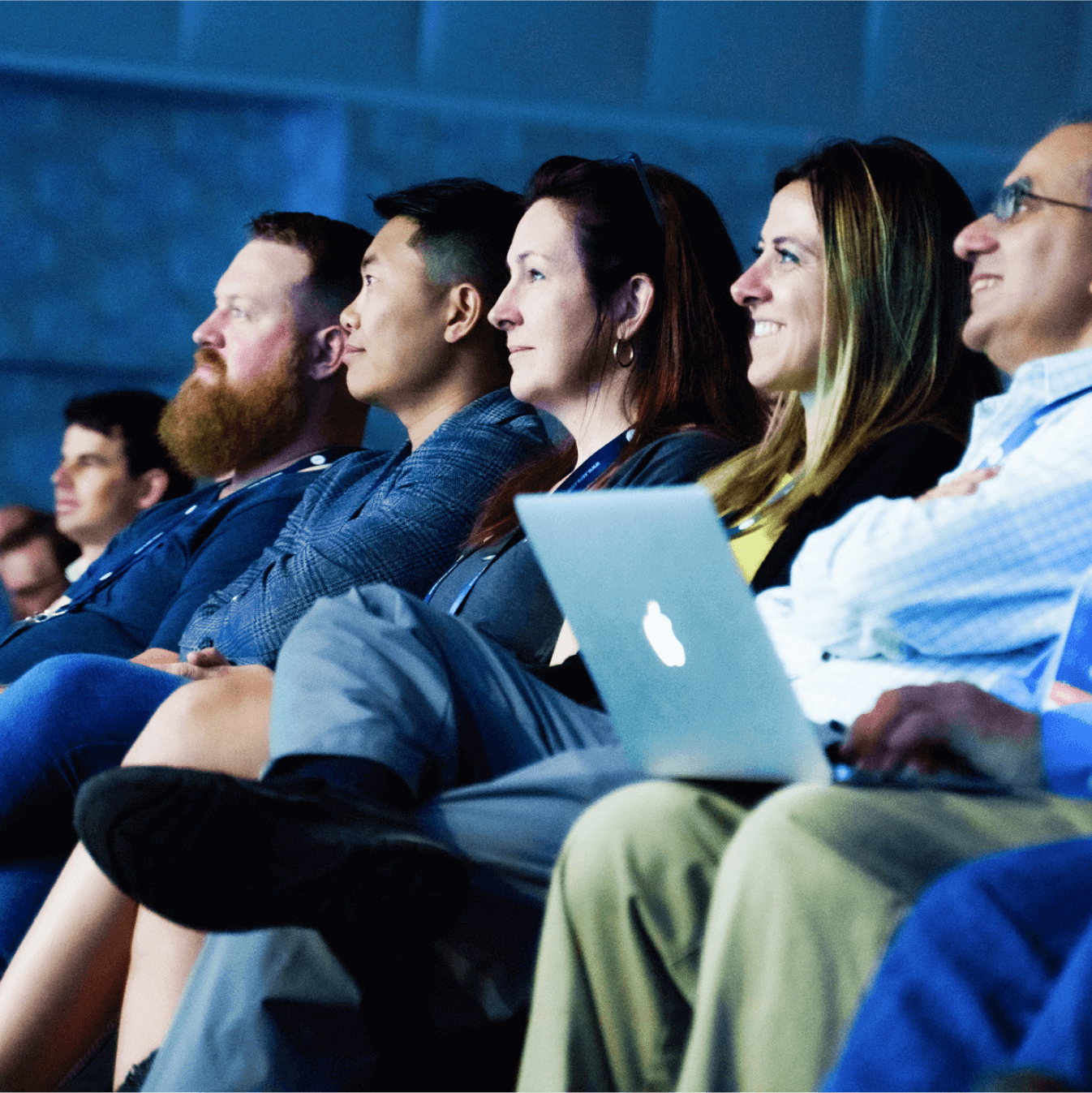 A row of people, one with a laptop on their lap, seated and watching a presentation.