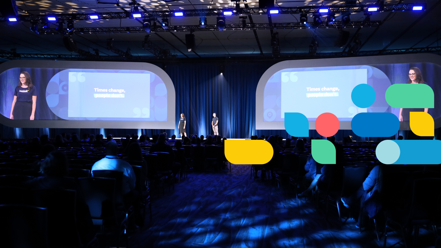 A presenter in a Xero t-shirt uses a remote control to operate a slide show. In the background is a colourful Xerocon graphic