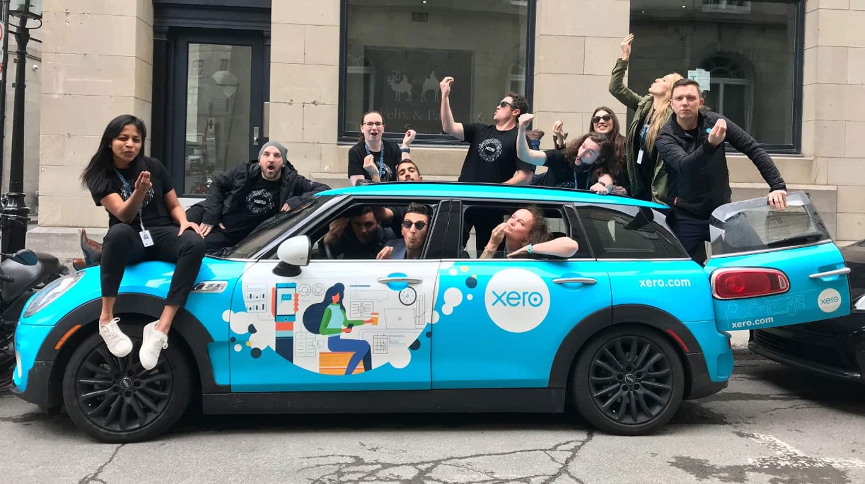 The Xero Wellington team and the Xero Canada team take a wacky pose in front of a Xero-branded car. 