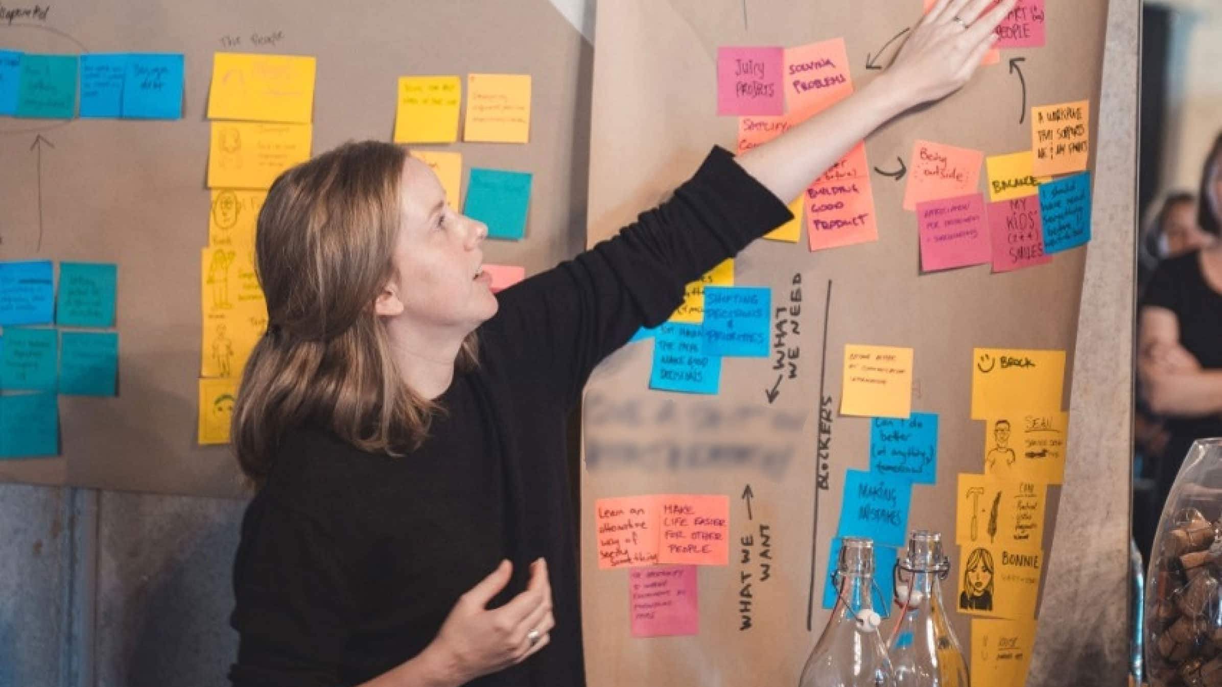 A design researcher reads one of the many coloured Post-it notes stuck onto a brown kraft paper.